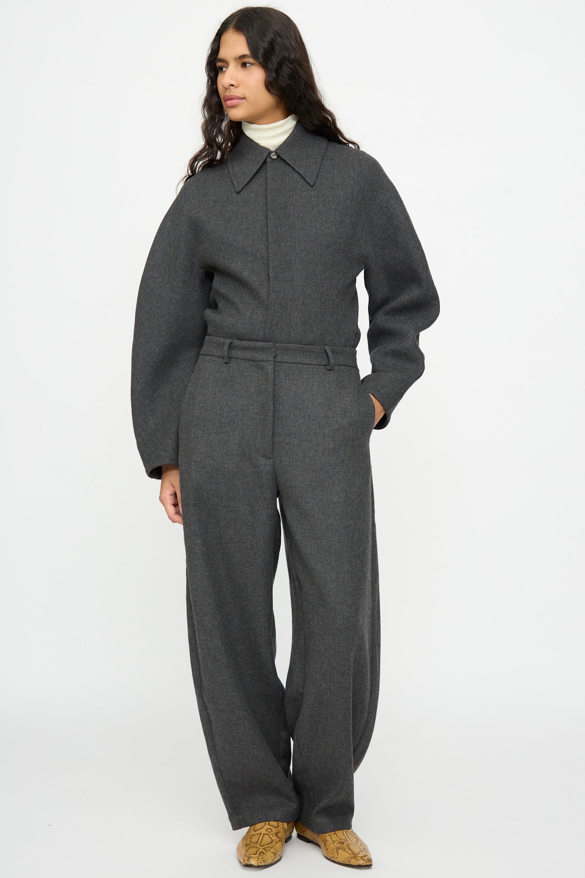 A person wearing a charcoal gray collared top, Cordera Wool Curved Pants in Anthracite, and snakeskin-patterned ankle boots.