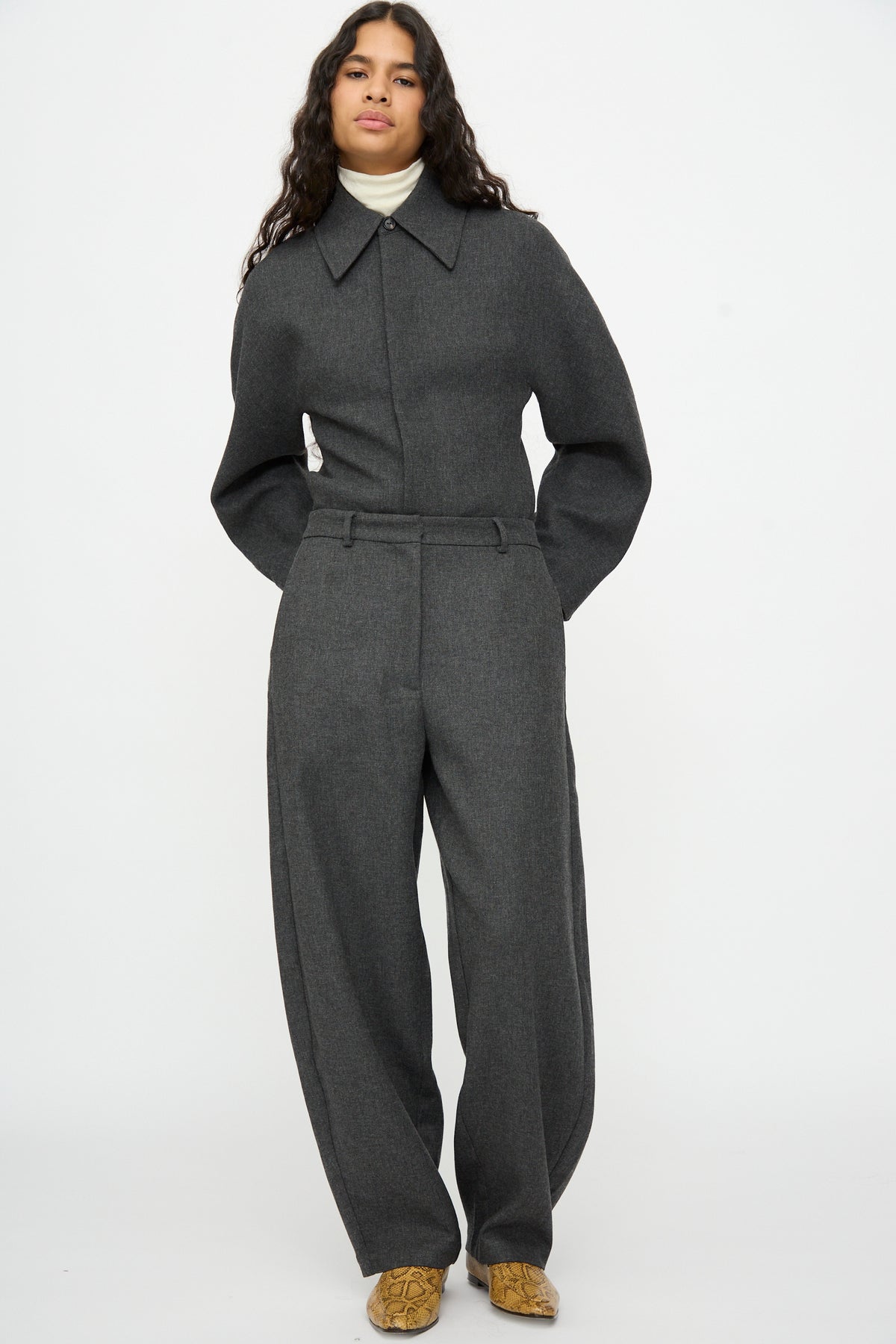 A person wearing a charcoal gray long-sleeved shirt with a pointed collar tucked into matching Cordera Wool Curved Pants in Anthracite.