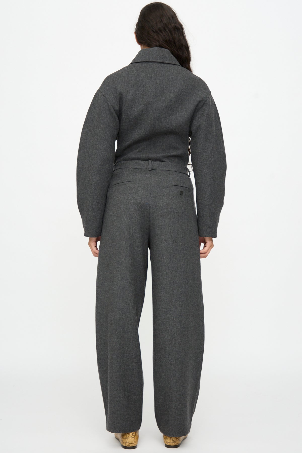 Back view of a person wearing a dark gray collared jacket and matching Wool Curved Pants in Anthracite, featuring a high-waisted, relaxed fit.