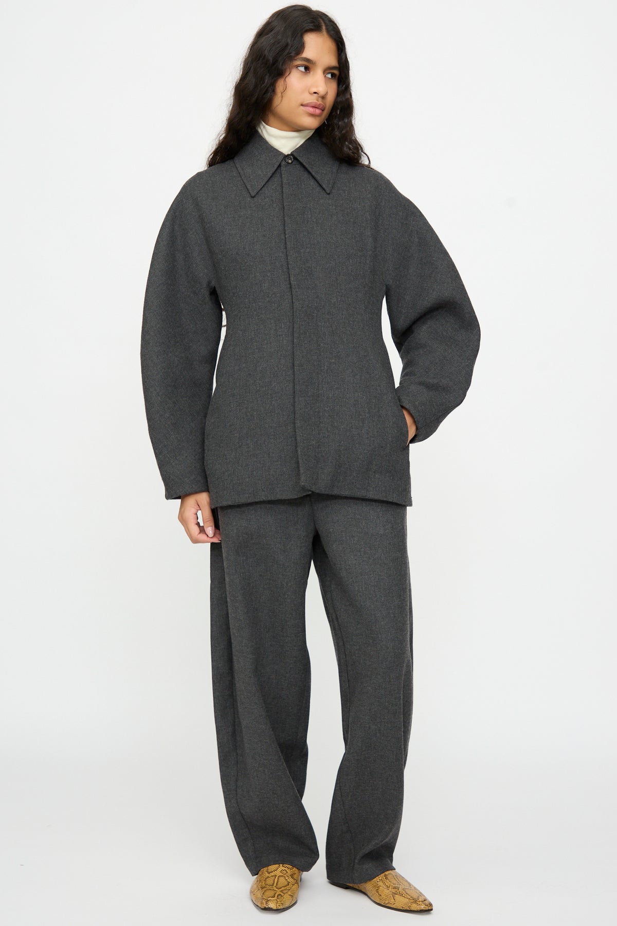 A person wearing a Cordera Wool Overshirt in Grey over matching trousers and a cream turtleneck.