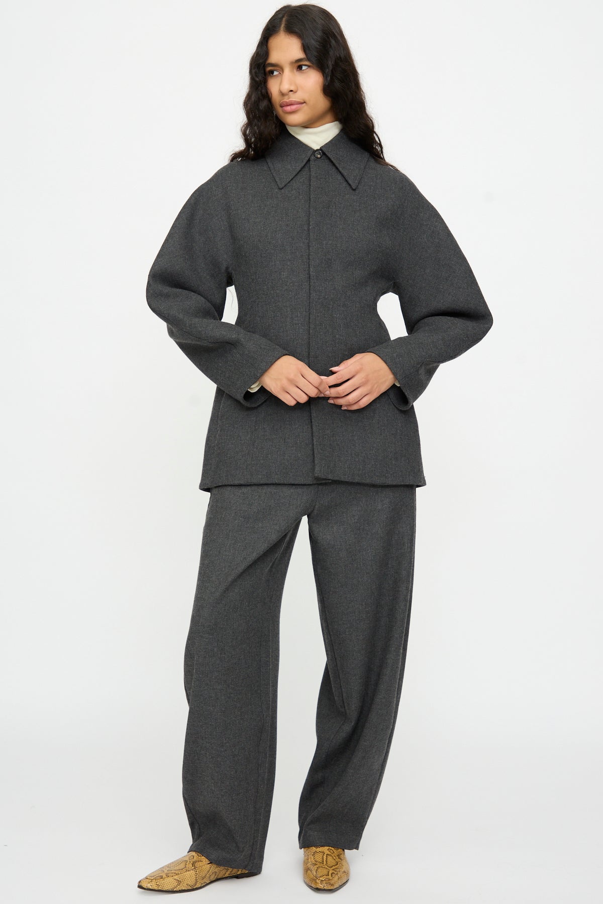 Person wearing a Cordera Wool Overshirt in Grey over matching wide-leg trousers, styled with rounded sleeves and beige snake-print shoes.