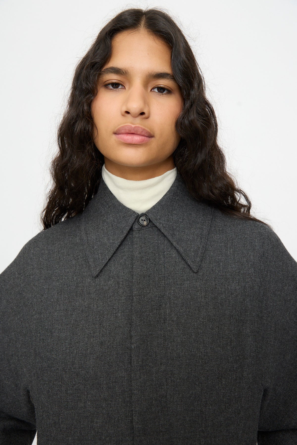 A person wearing a relaxed fit, grey Cordera Wool Overshirt over a cream-colored mock neck top.