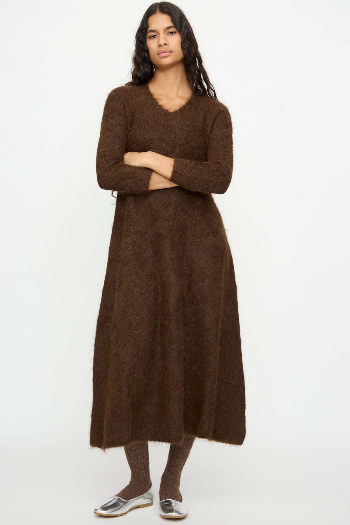A person wears a brown Cosmic Wonder Alpaca Knitted Evening Dress, styled with long sleeves, midi length, brown tights, and silver flats.