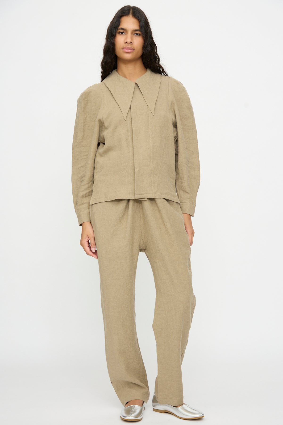 A person wearing a beige Cosmic Wonder Band Collar Shirt with an oversized pointed collar and matching trousers.