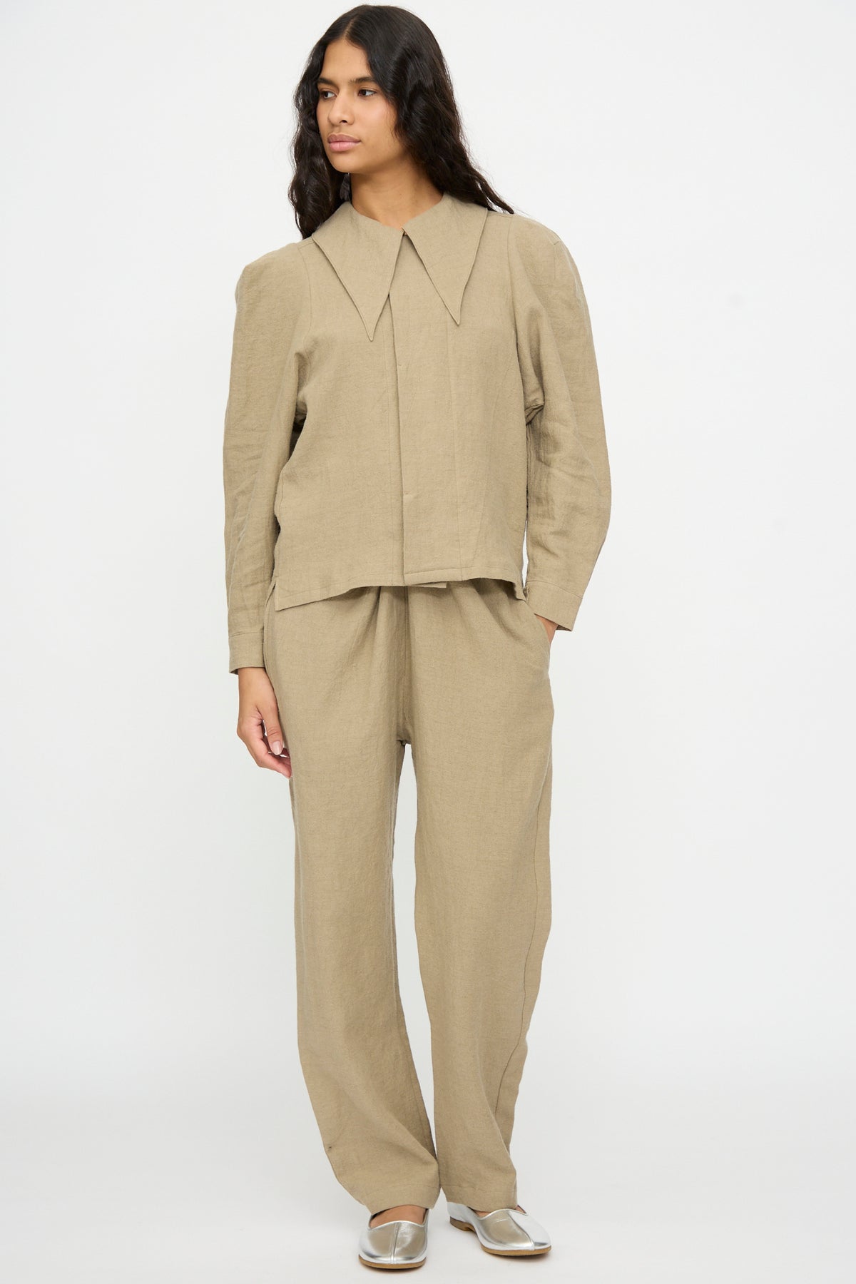 A person wearing a Cosmic Wonder Band Collar Shirt in beige and matching linen wool trousers.