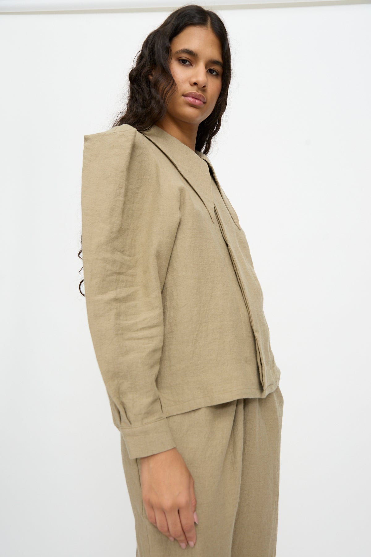 A person wearing a Cosmic Wonder Band Collar Shirt in beige, featuring a long-sleeved linen wool design with a wide collar and structured shoulders.