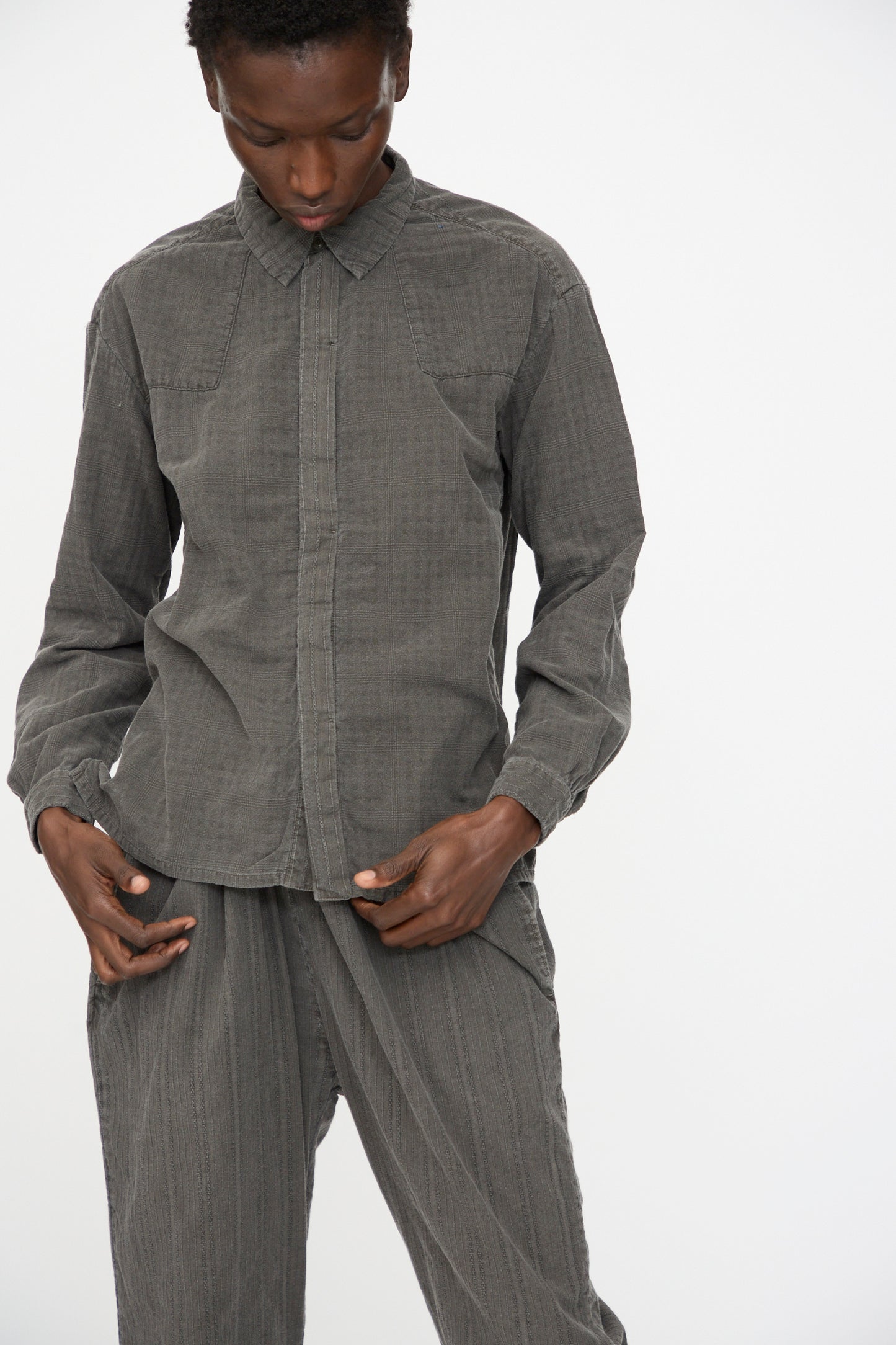 Person wearing the Cosmic Wonder Double Gauze Check Country Shirt in Dark Sumi, paired with matching pants, looking down with hands near waist against a plain white background.