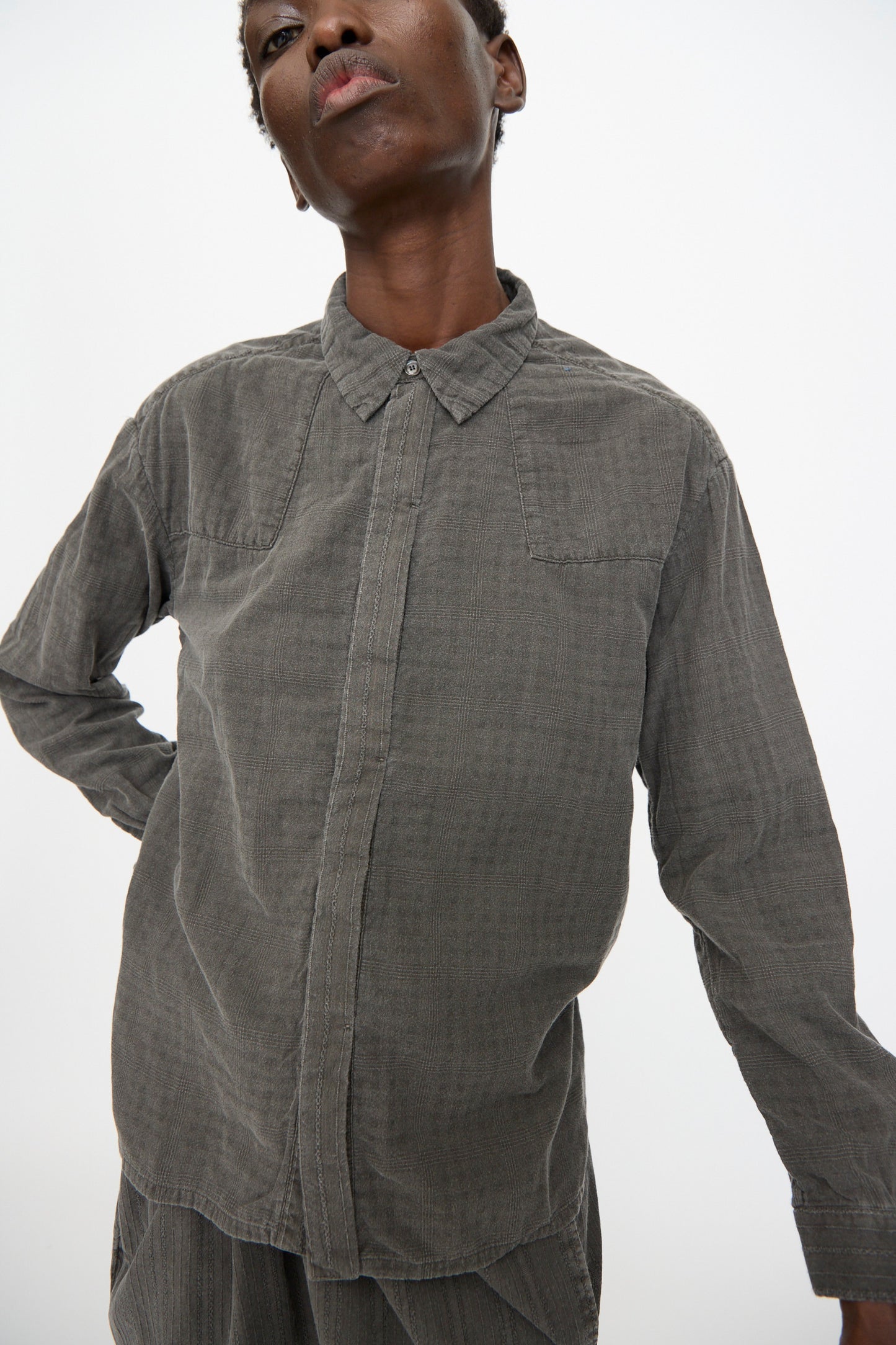 A person wears the Cosmic Wonder Double Gauze Check Country Shirt in Dark Sumi, featuring a collar and button-up design, standing against a plain white background.
