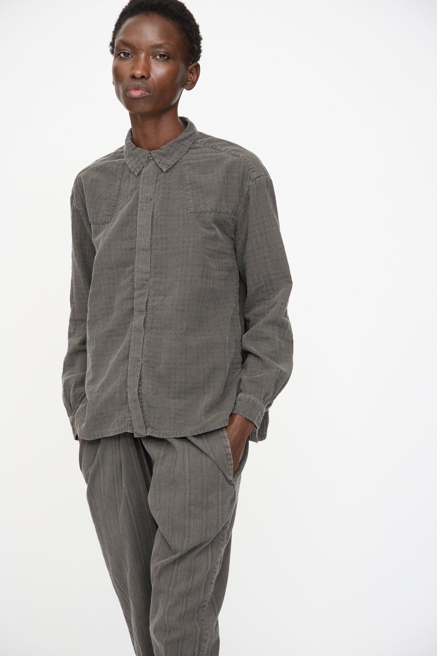 A person wears the Cosmic Wonder Double Gauze Check Country Shirt in Dark Sumi, styled loosely and casually with hands in pockets, standing against a plain white background.