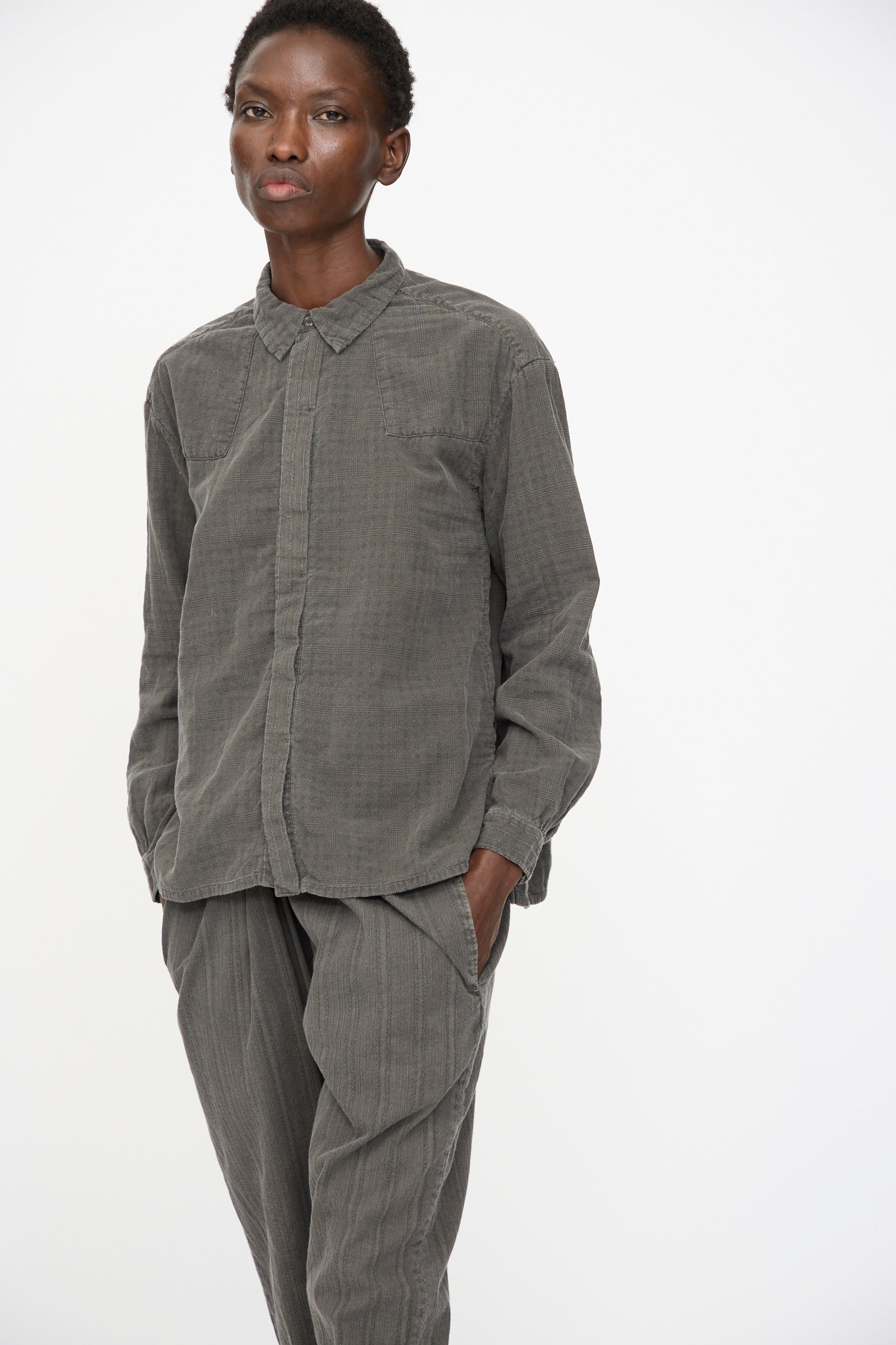A person wears the Cosmic Wonder Double Gauze Check Country Shirt in Dark Sumi, styled loosely and casually with hands in pockets, standing against a plain white background.