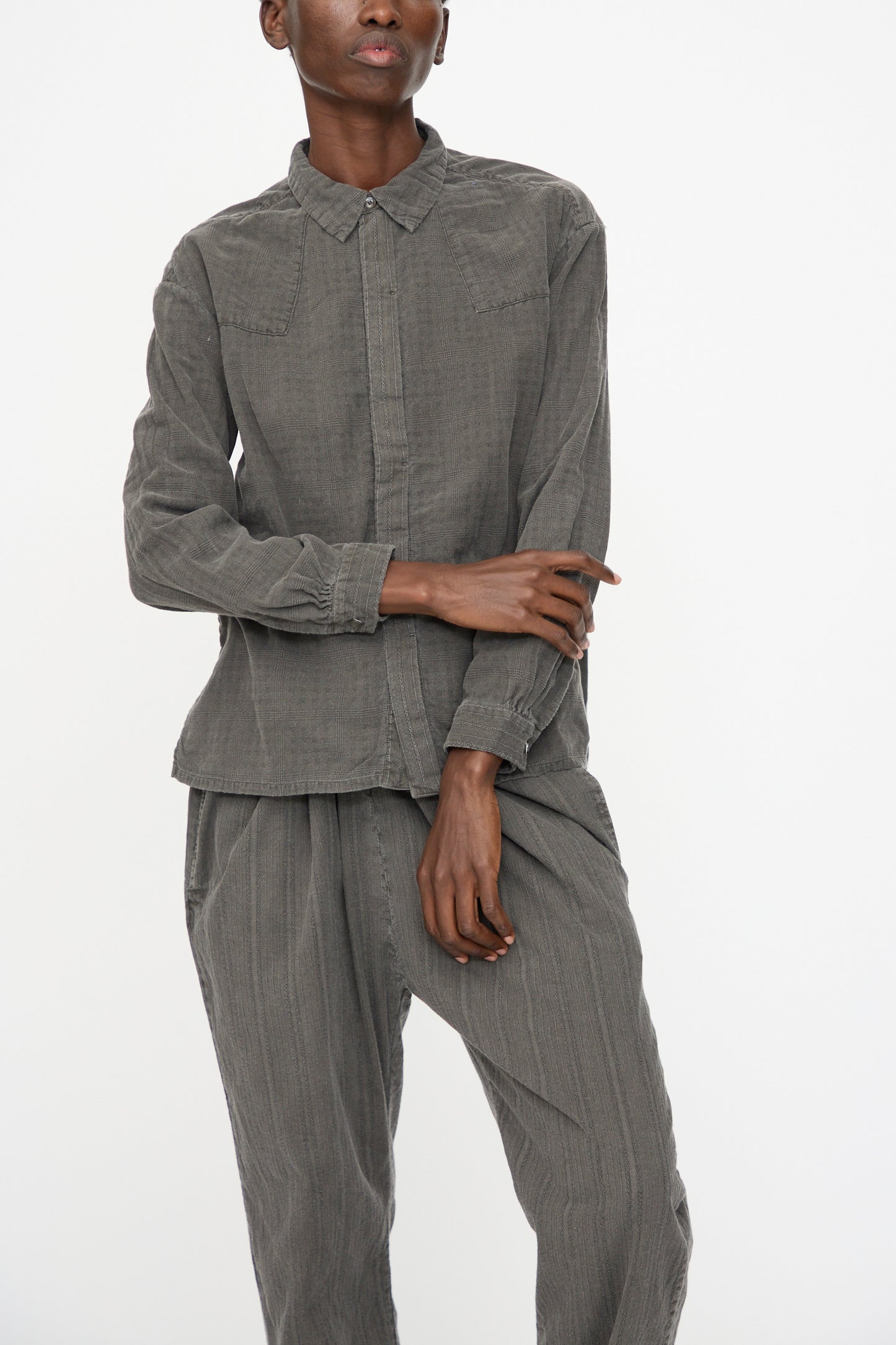 A person wears the Cosmic Wonder Double Gauze Check Country Shirt in Dark Sumi, a button-up, long-sleeve gray shirt made in Japan, paired with matching gray pants, standing against a plain white background.