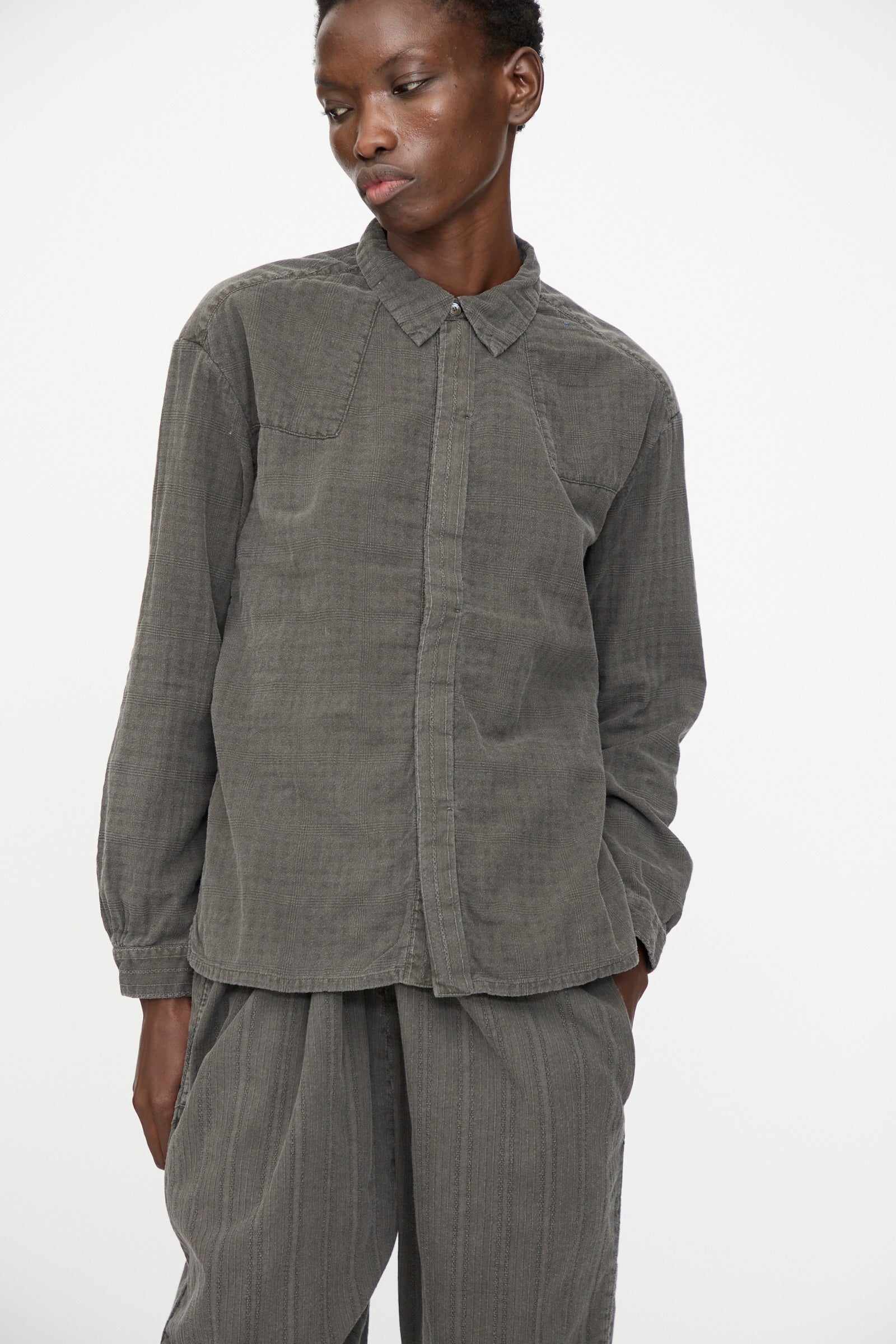 A person wears the Cosmic Wonder Double Gauze Check Country Shirt in Dark Sumi, standing against a plain white background with one hand in their pocket.