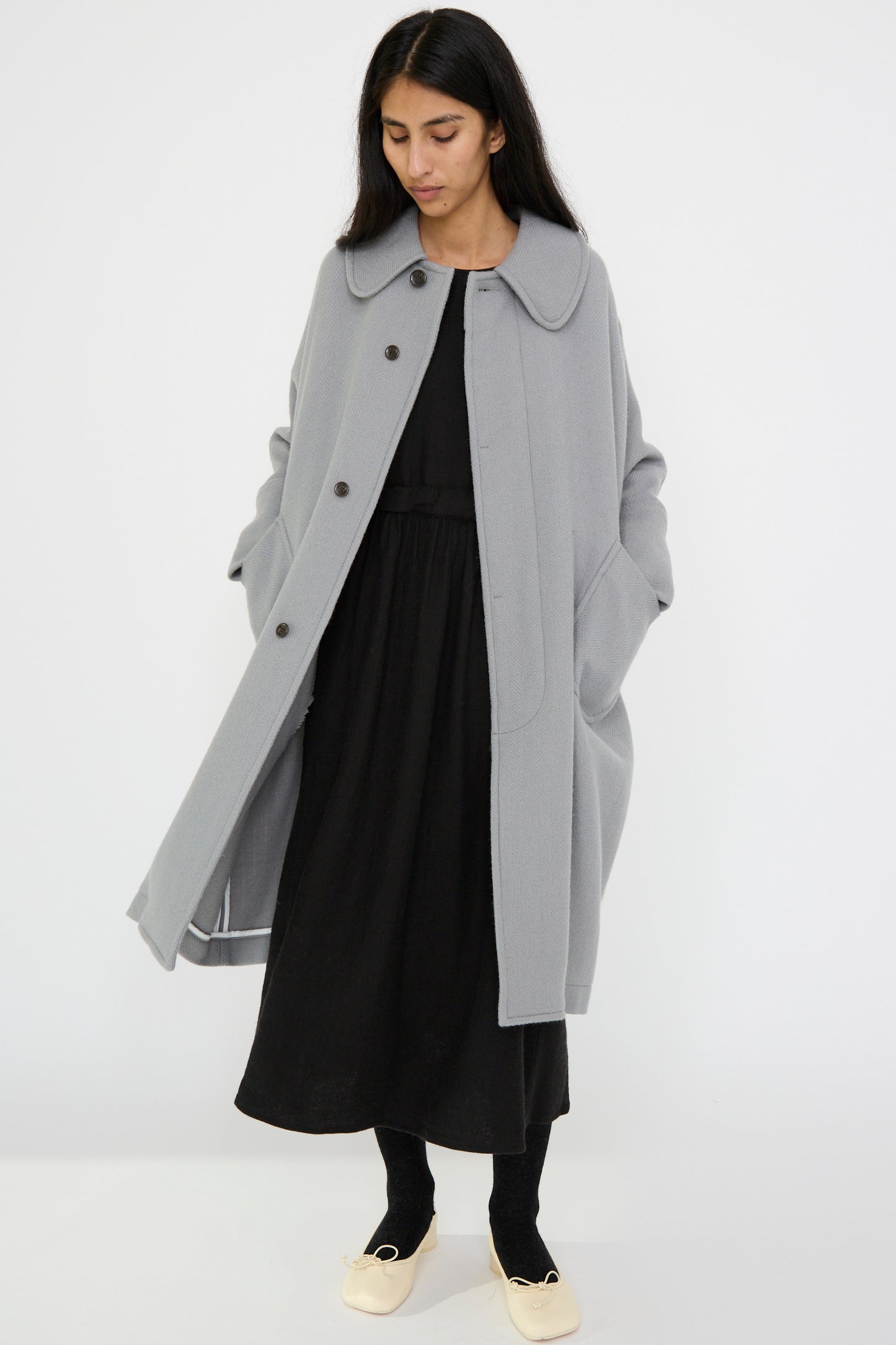 A person wearing the Herringbone Shetland Wool Dolman Sleeve Coat in Gray by Cosmic Wonder over a black dress stands against a plain white background.