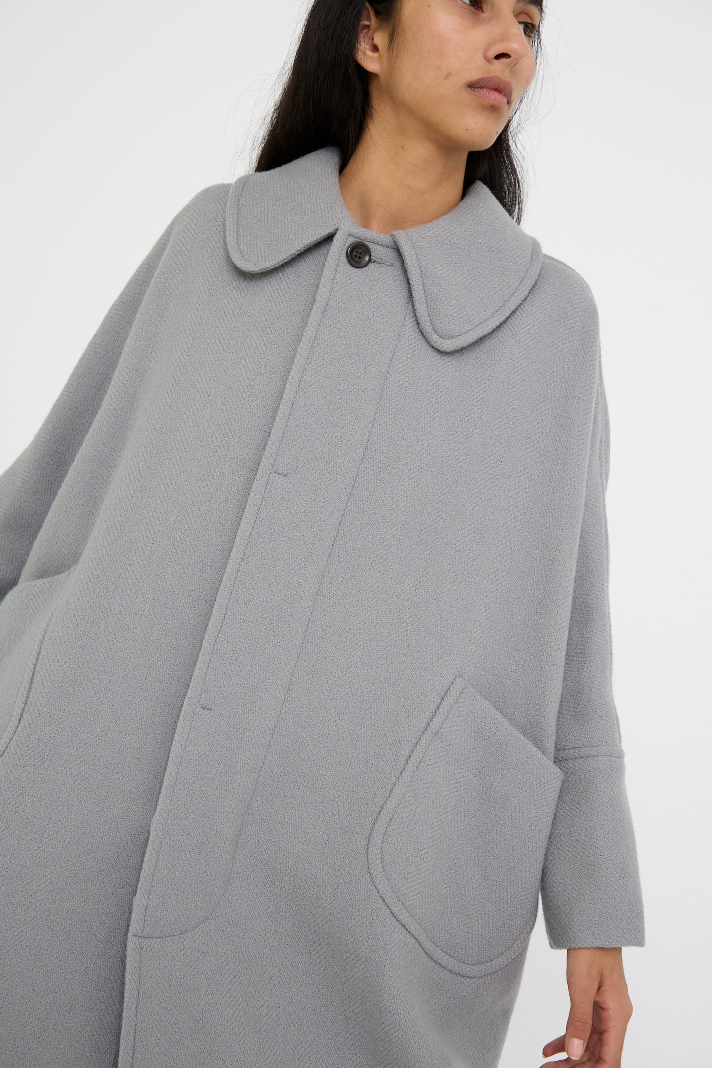 A person models the Cosmic Wonder Herringbone Shetland Wool Dolman Sleeve Coat in gray against a plain background, showcasing its large collar and pocket details.