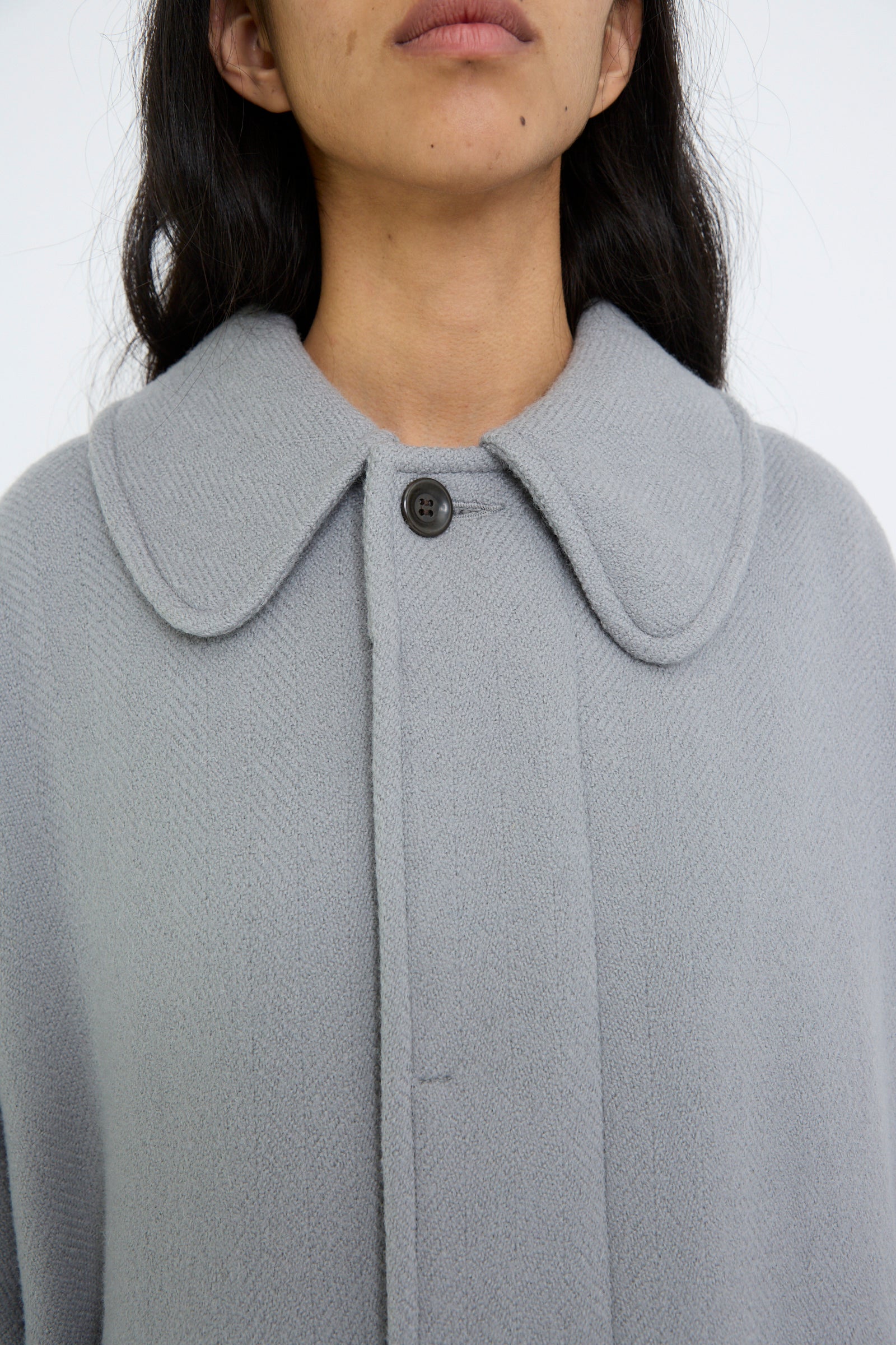 A close up of a person wearing the Herringbone Shetland Wool Dolman Sleeve Coat in Gray by Cosmic Wonder, featuring an oversized design with a large collar and a button at the top.