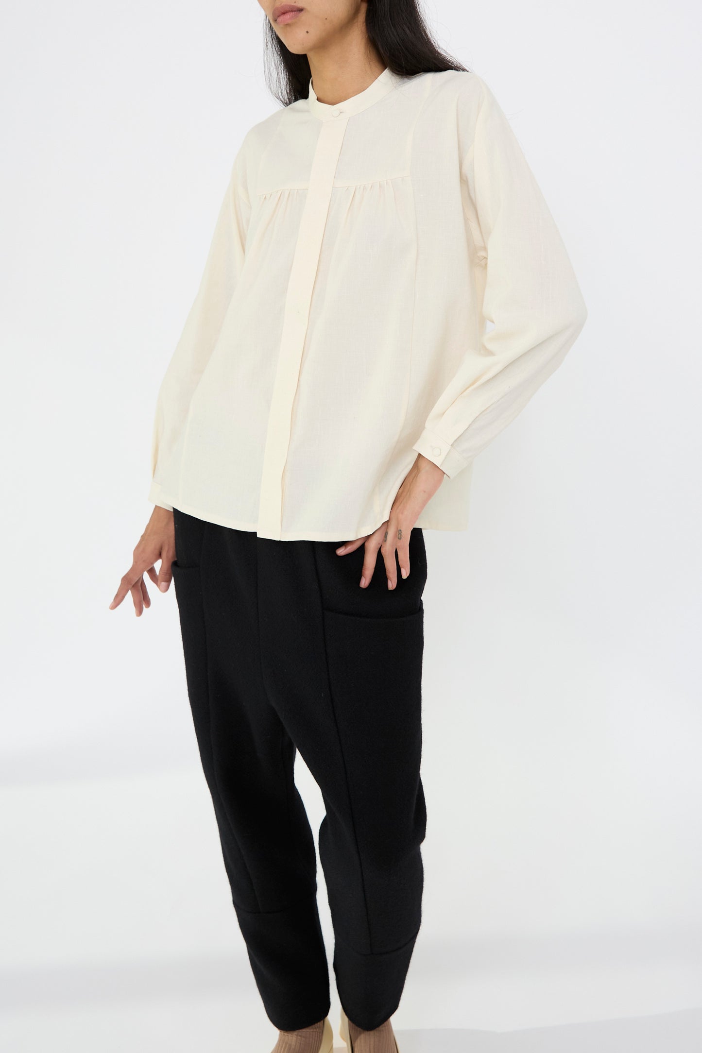 A person is dressed in a white, long-sleeve gathered shirt from Cosmic Wonder with black pants, standing against a white background.