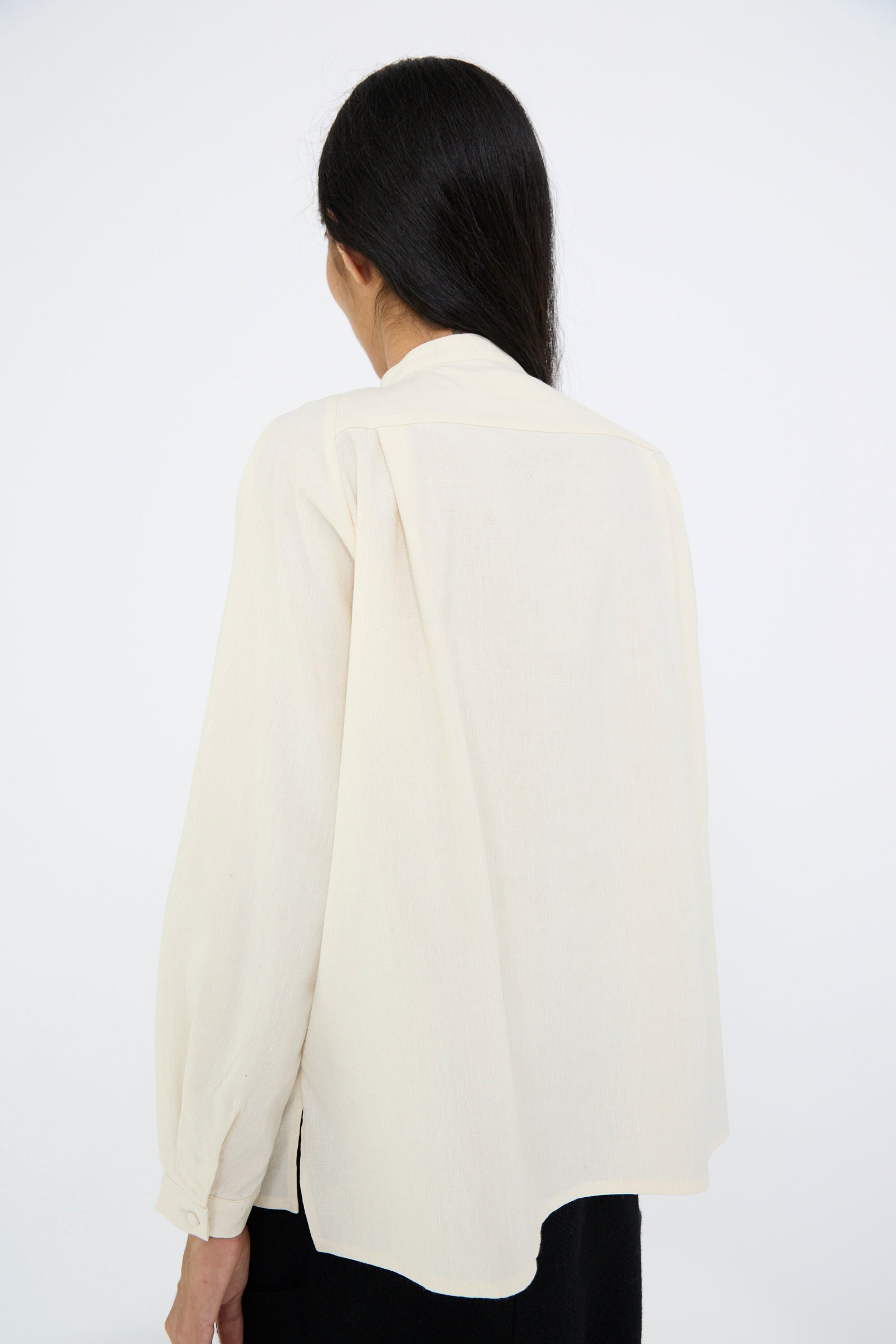 A person with long dark hair is wearing the Light Merino, Linen and Cotton Glencheck Elegant Gathered Shirt in White by Cosmic Wonder, standing with their back to the camera against a plain background.