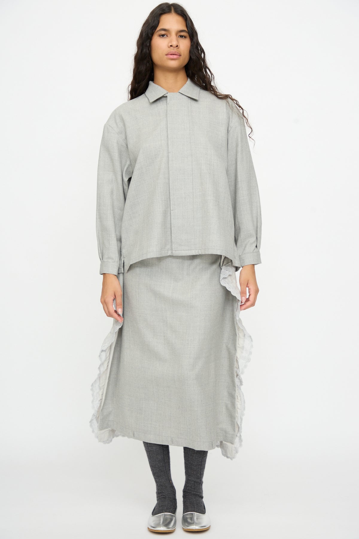 A person wearing a gray wool Nostalgic Artist’s Camp Collar Shirt with a matching midi skirt with ruffled side panels over dark gray leggings and silver flats.