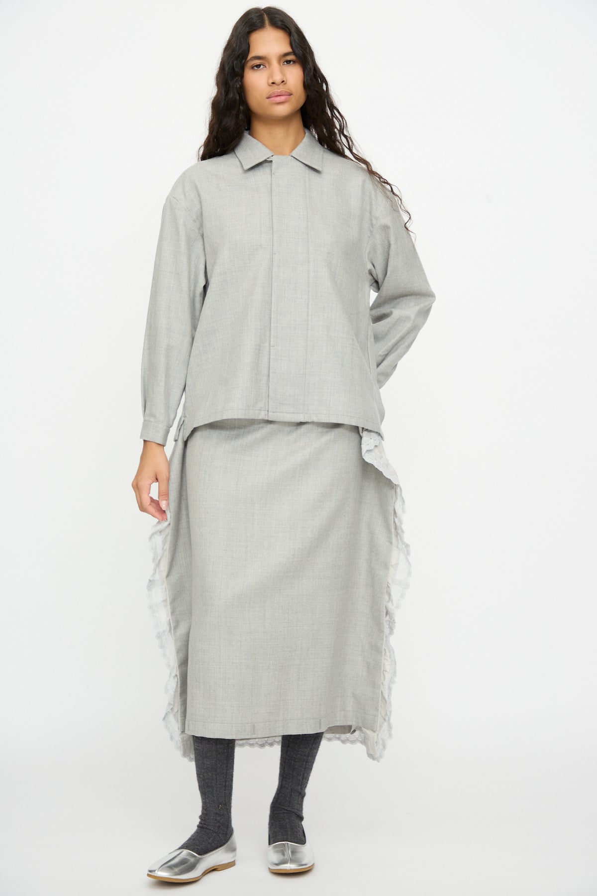 A person wears a Cosmic Wonder Nostalgic Artist’s Camp Collar Shirt in Gray with a matching midi skirt featuring lace-trimmed side vents, dark leggings, and metallic silver shoes.