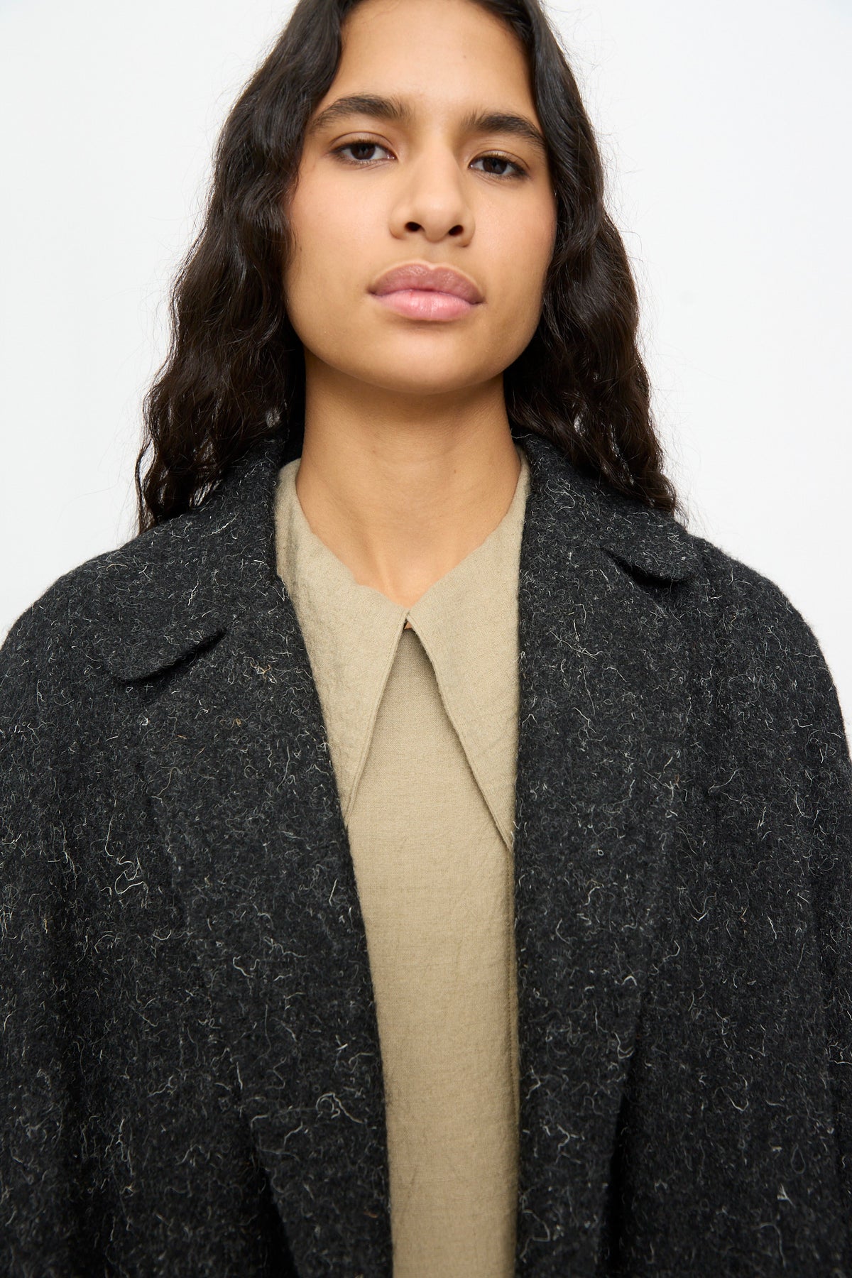 A person wearing an oversized, textured, dark gray Cosmic Wonder Nostalgic Painter’s Winter Coat in Black over a beige collared shirt.