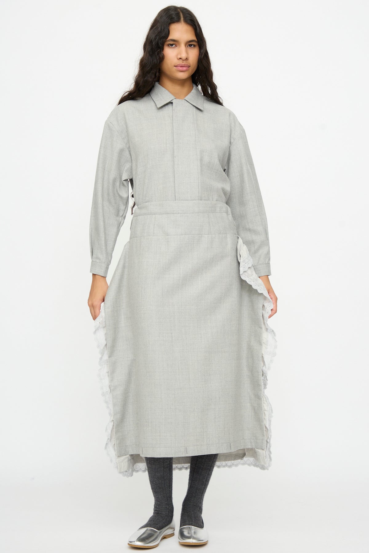 A person wears a gray, made-in-Japan Cosmic Wonder Nostalgic Painter’s Work Skirt with an adjustable-waist, lace-trimmed midi apron, dark leggings, and silver flat shoes.