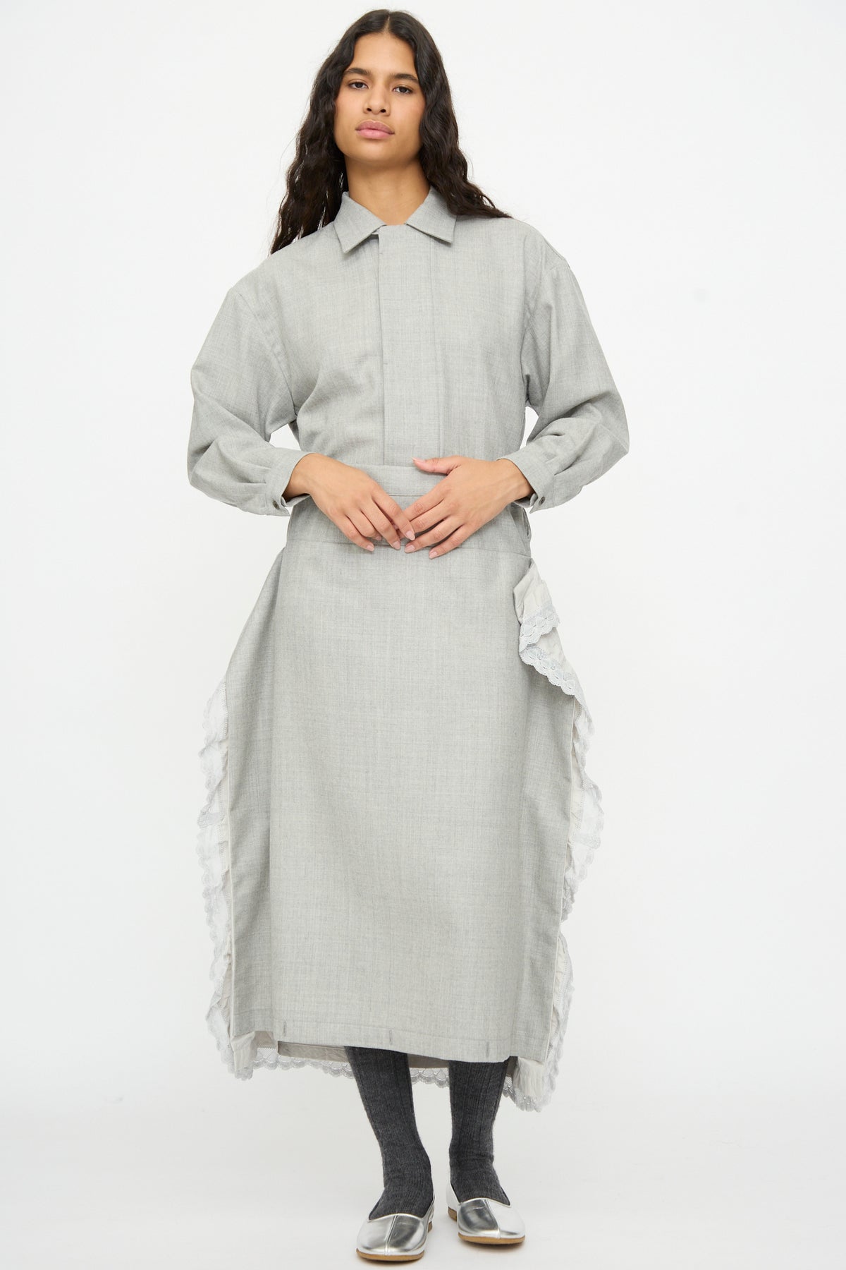 A model wears a gray Cosmic Wonder Nostalgic Painter’s Work Skirt midi dress with ruffled white trim, styled with dark leggings and silver shoes.
