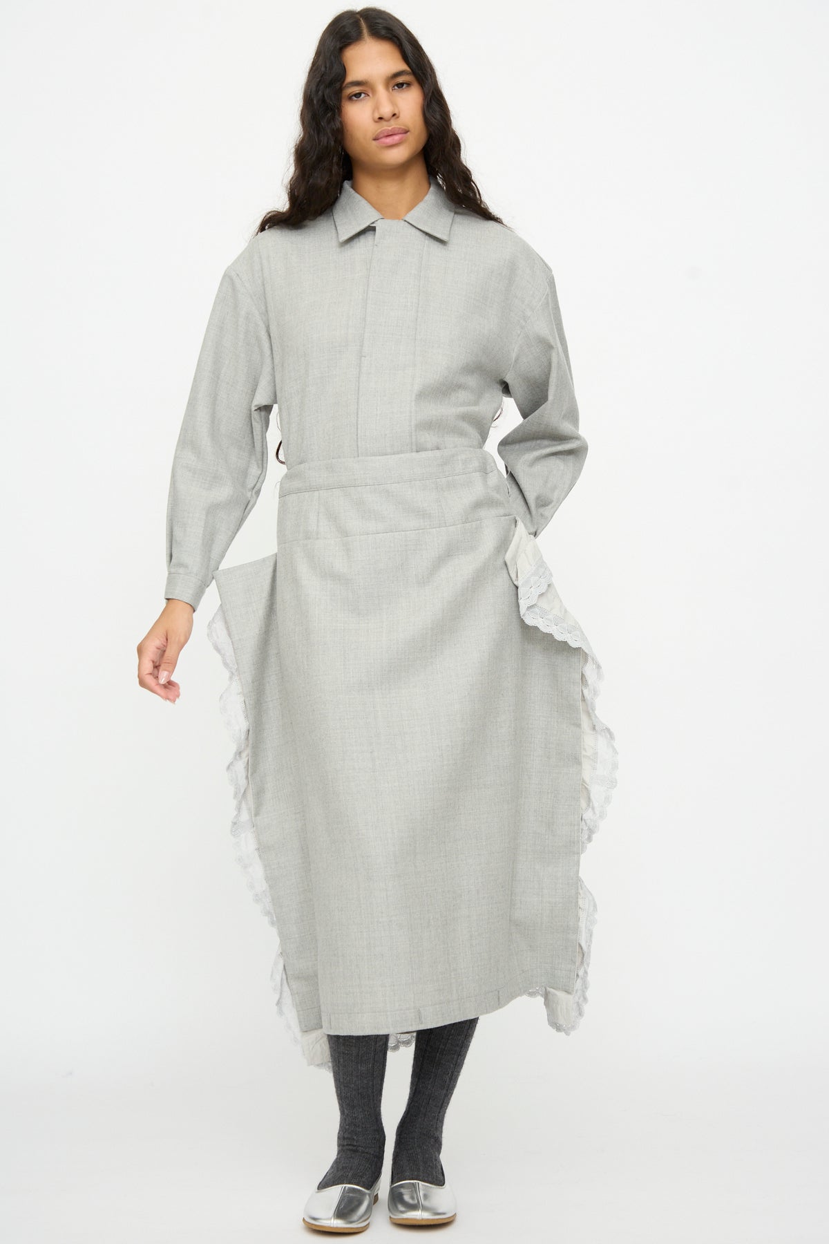A person wears a Cosmic Wonder Nostalgic Painter’s Work Skirt in Gray, styled as a long-sleeved gray collared midi dress with a layered, apron-style skirt featuring ruffled white lace trim.