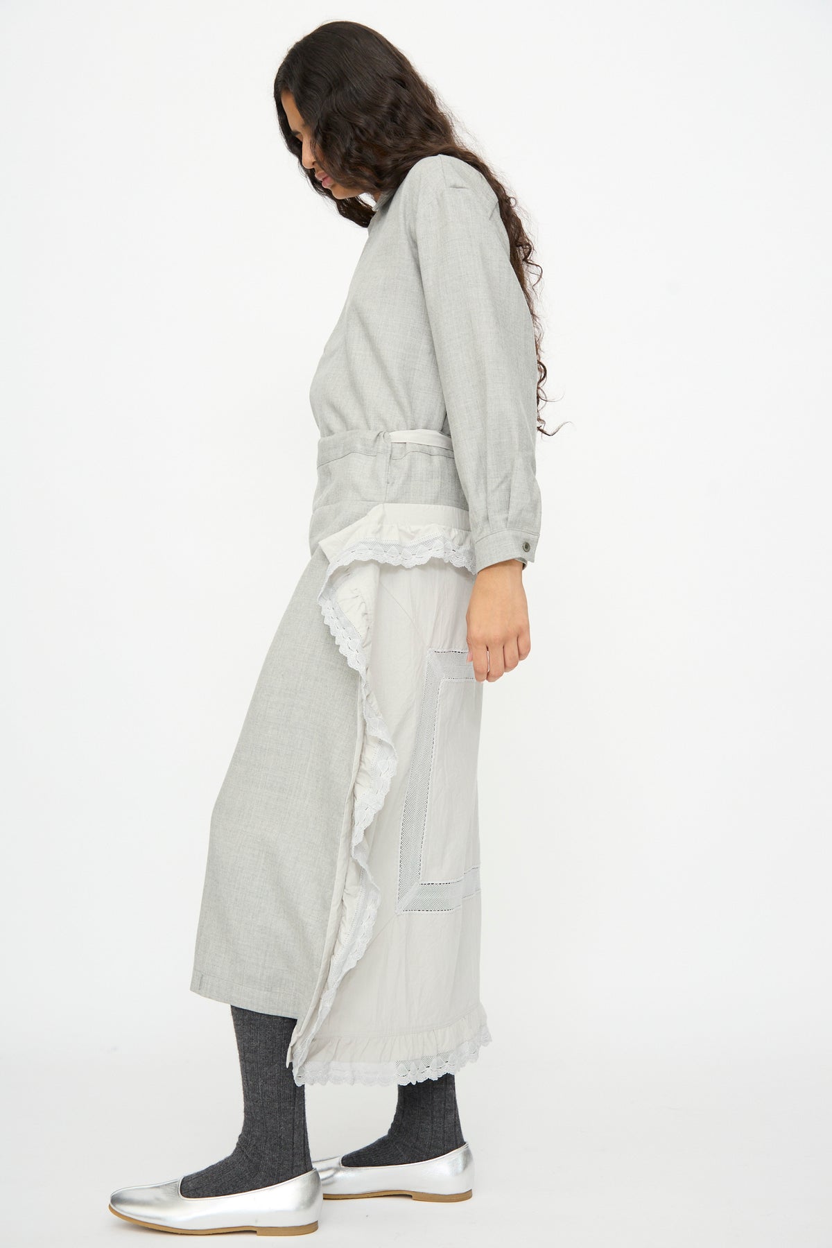 A person wearing a gray long-sleeved shirt and a Cosmic Wonder Nostalgic Painter’s Work Skirt in Gray with white lace trim, paired with dark leggings and silver flats.