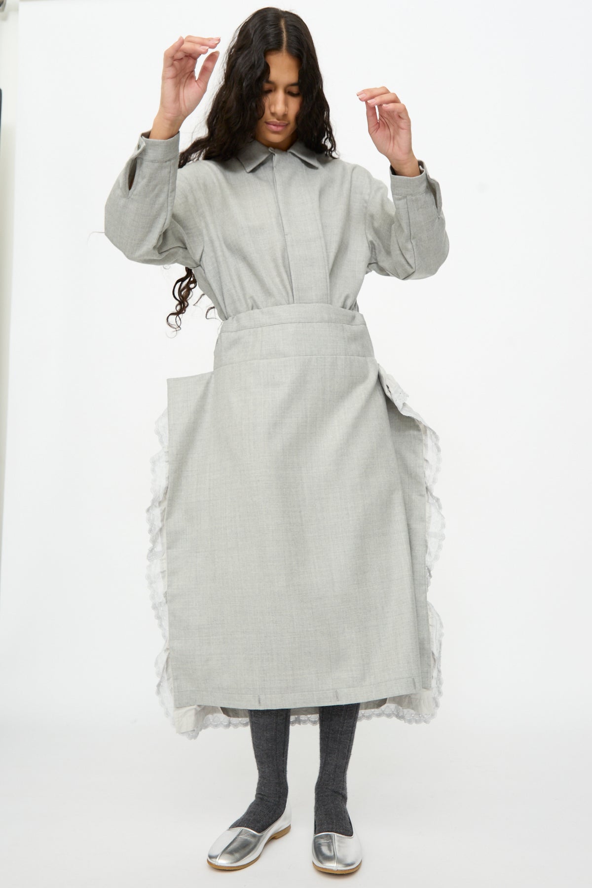 A person wears a gray button-up shirt and a Cosmic Wonder Nostalgic Painter’s Work Skirt in Gray with ruffled sides over gray leggings and silver flats.