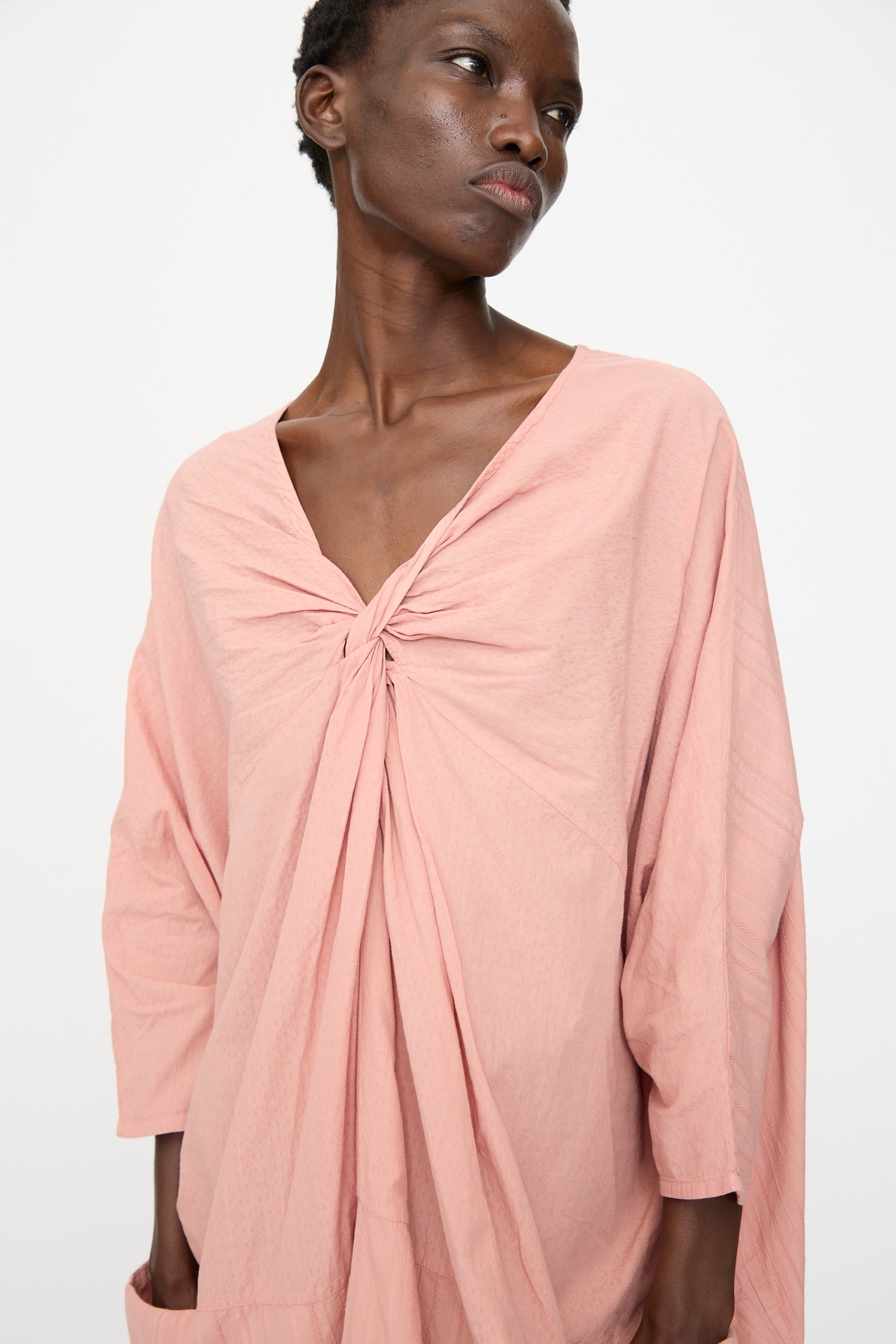A person wearing the Cosmic Wonder Stripe Combination Twisted Dress in Rose Crystal, featuring a loose fit and knotted neckline, stands against a plain white background.