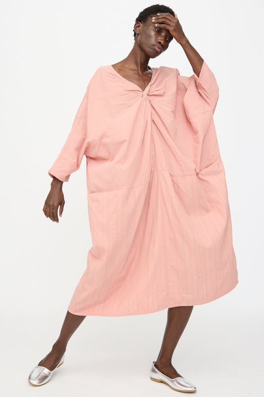 Model wearing the Stripe Combination Twisted Dress in Rose Crystal by Cosmic Wonder, a relaxed fit, knee-length pink dress with long sleeves, paired with silver shoes against a plain white background.