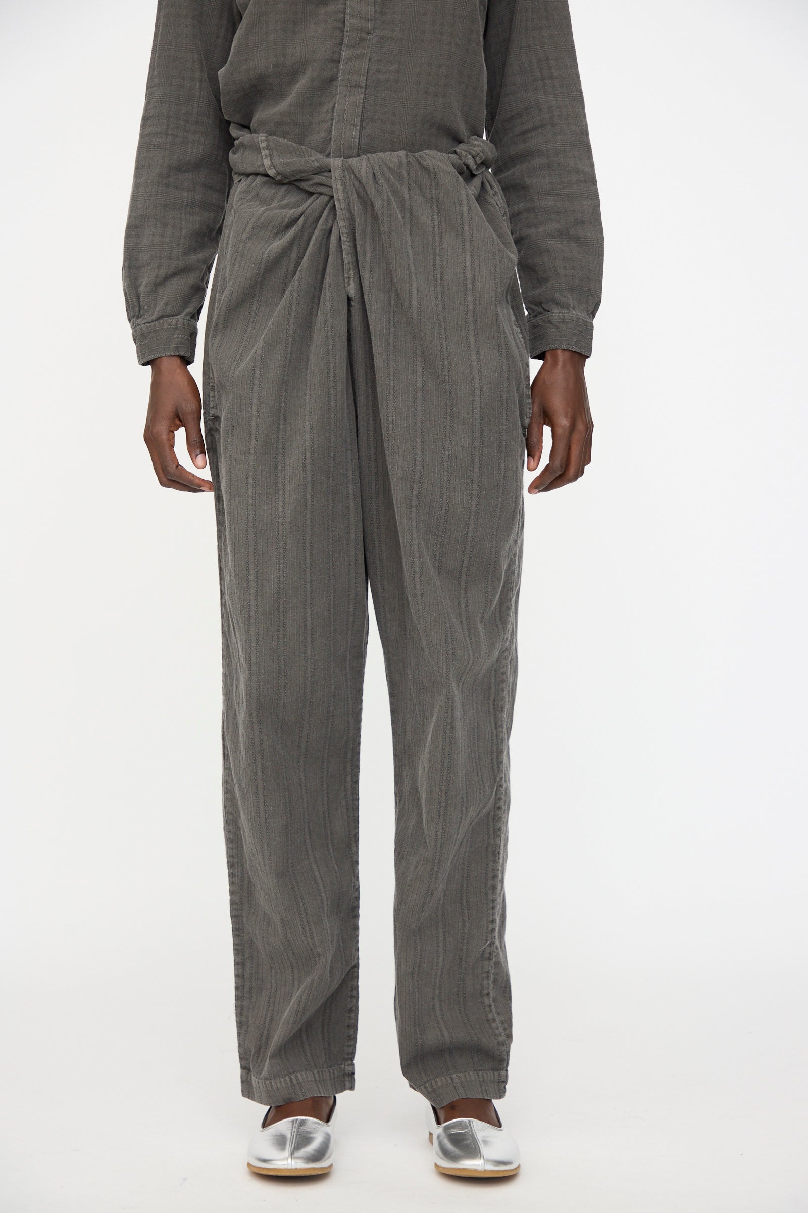 A person models Cosmic Wonder's Stripe Combination Wrapped Pant in Dark Sumi with a matching top and silver slip-on shoes, standing against a plain white background.