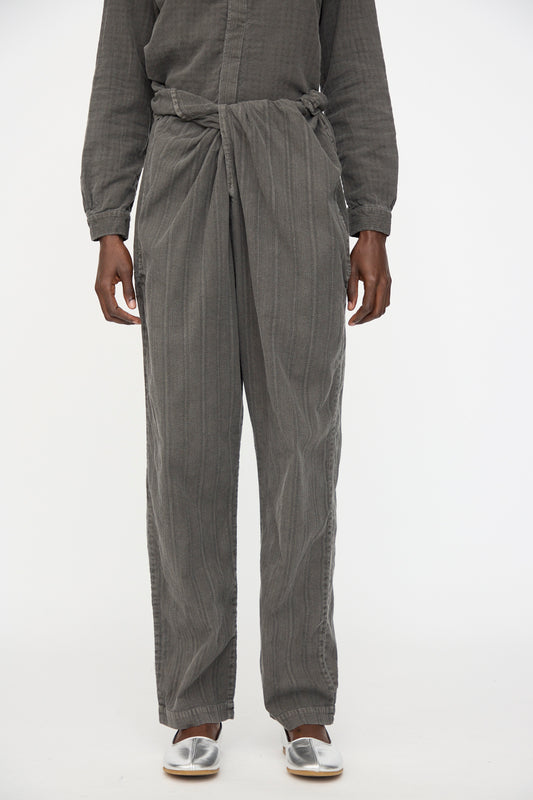 A person models Cosmic Wonder's Stripe Combination Wrapped Pant in Dark Sumi with a matching top and silver slip-on shoes, standing against a plain white background.
