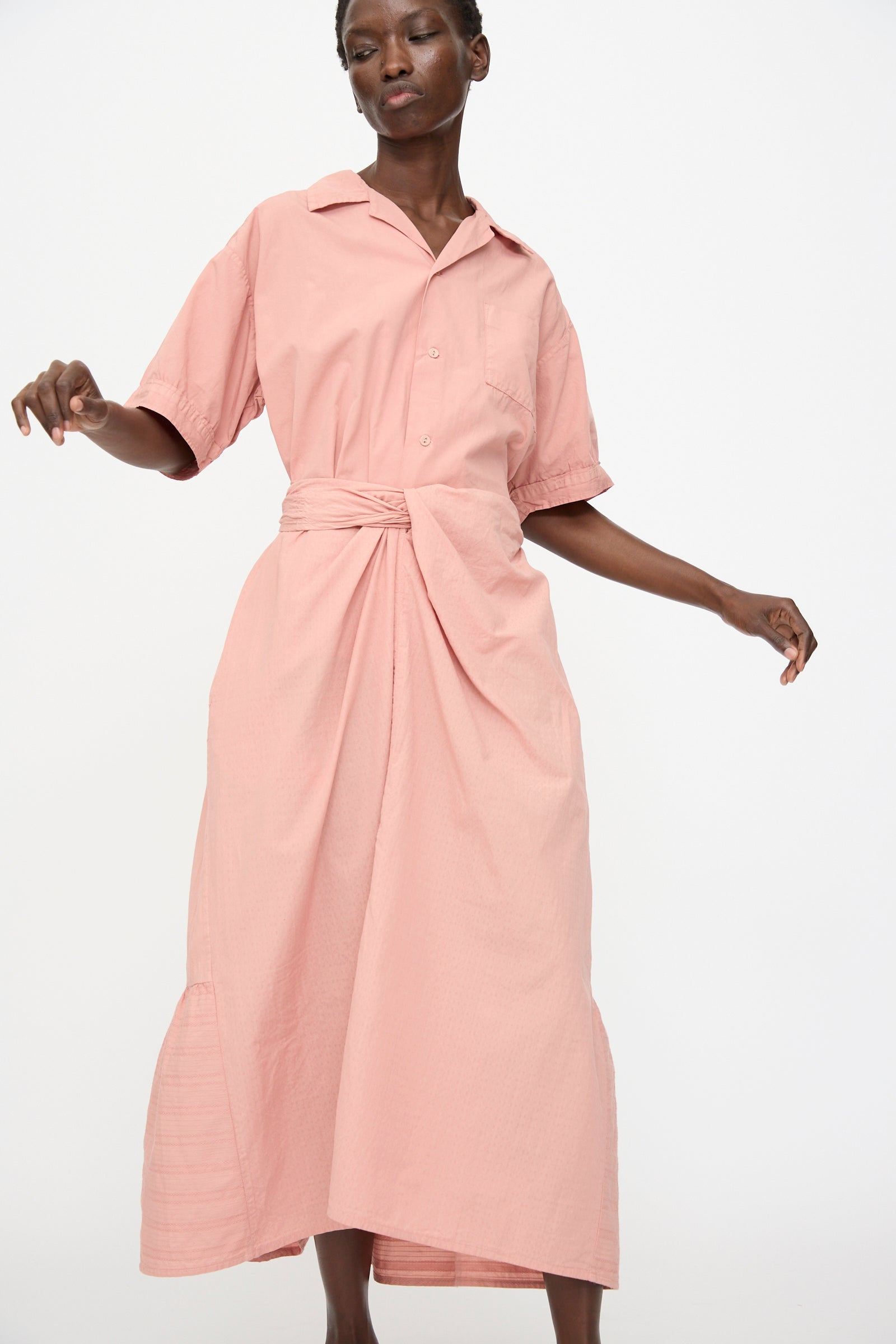 A person wearing the Cosmic Wonder Stripe Combination Wrapped Skirt in Rose Crystal, featuring a light pink hue and long silhouette, stands against a plain white background.