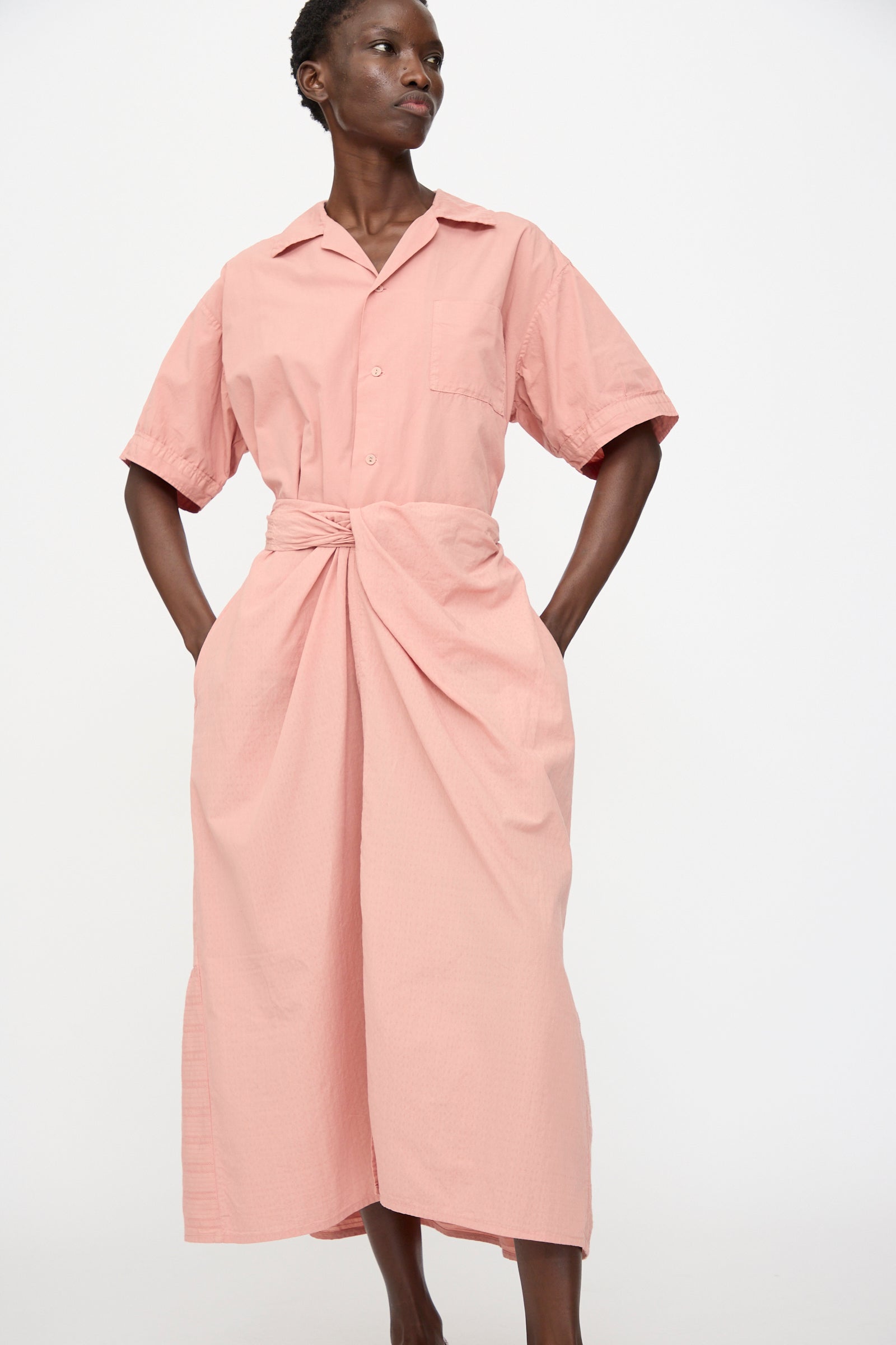A person stands against a plain background wearing Cosmic Wonder's Stripe Combination Wrapped Skirt in Rose Crystal, a short-sleeve button-up dress with an organic cotton skirt, wrapped design, and collar.