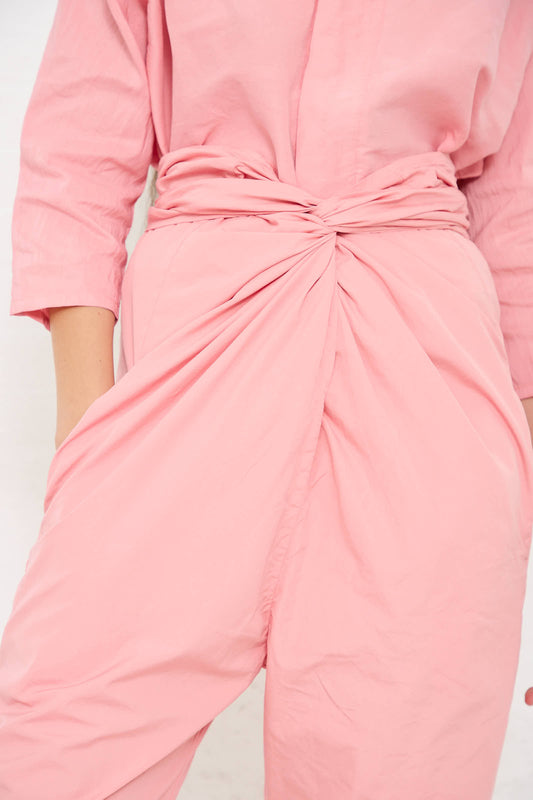 A close-up of a person wearing a crinkled pink **Suvin Cotton Broadcloth Pant in Peach Jade** by **Cosmic Wonder** with an adjustable tie waist and their hands in the pockets.