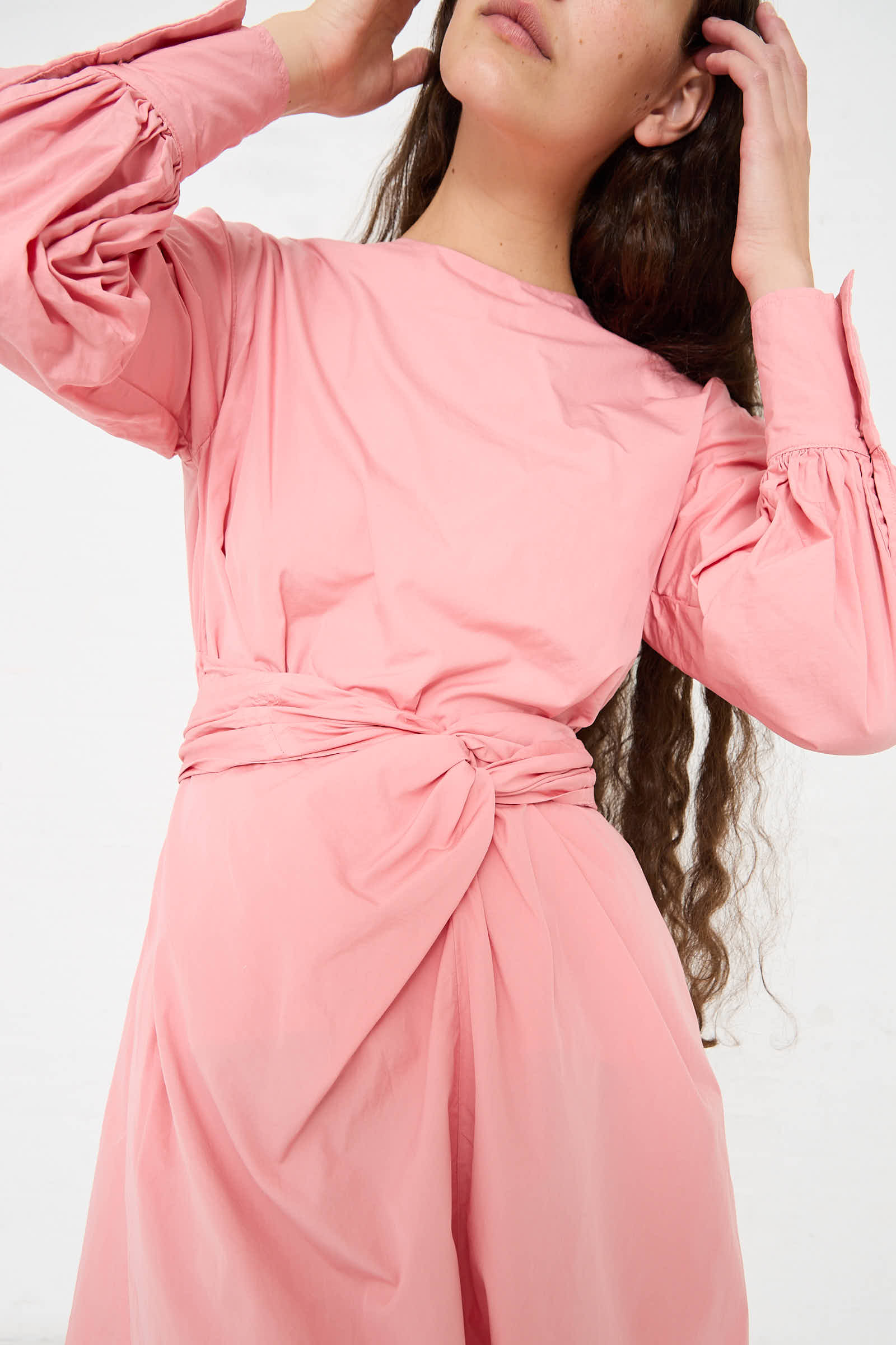 A person in a Suvin Cotton Broadcloth Wrapped Dress in Peach Jade by Cosmic Wonder, adjusting their hair.