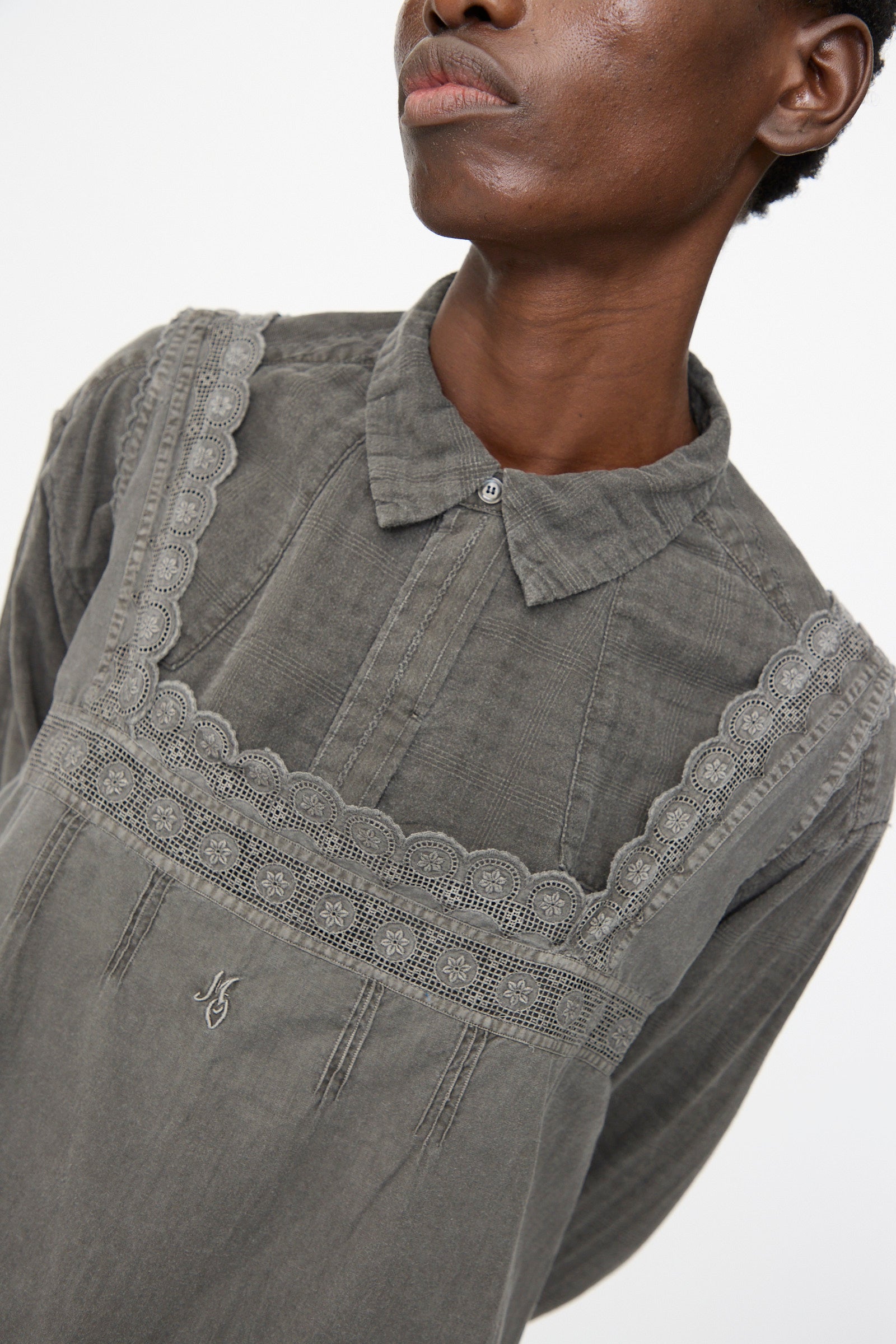 A person wearing the Cosmic Wonder Taskuki Apron in Dark Sumi, a gray collared shirt with decorative lace-trimmed overlay inspired by antique undergarments, shown from the shoulders up against a plain background.