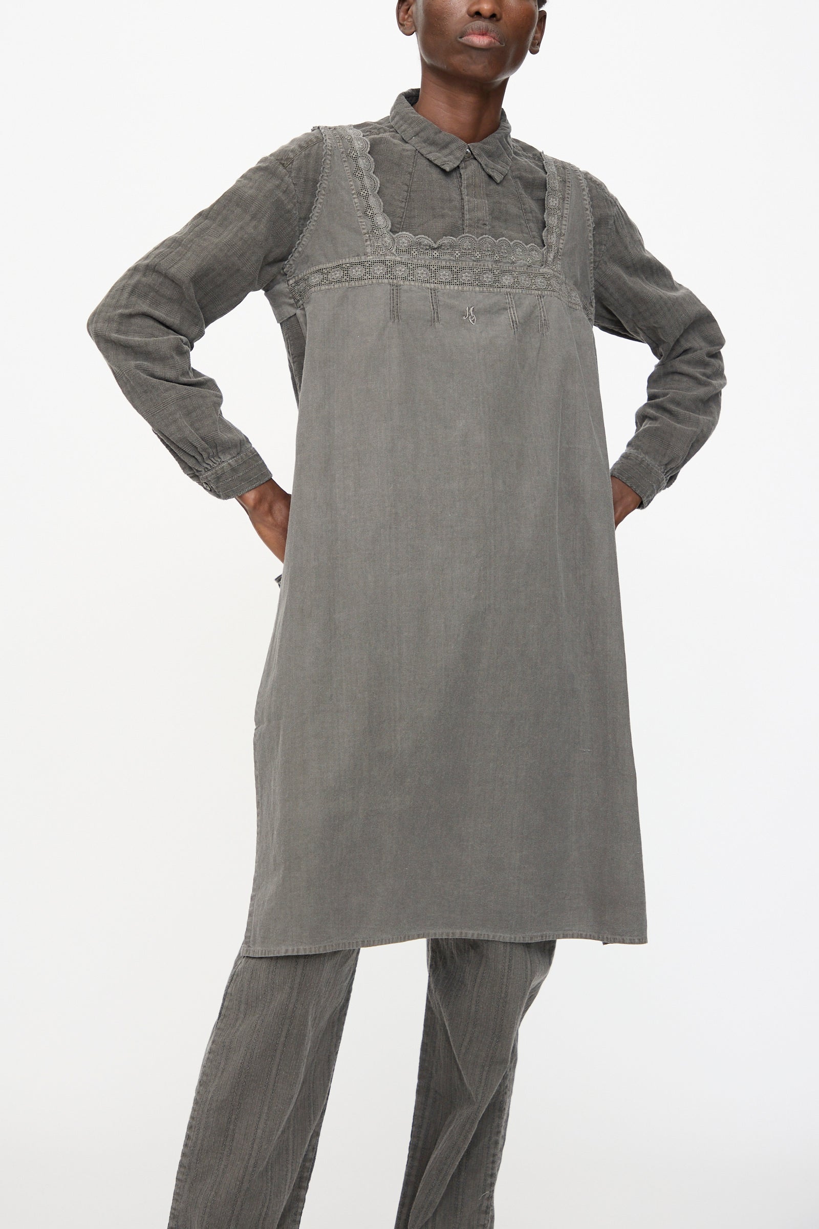 Against a plain white background, a person stands with hands on hips, wearing the Cosmic Wonder Taskuki Apron in Dark Sumi over a long-sleeved collared shirt and matching pants.