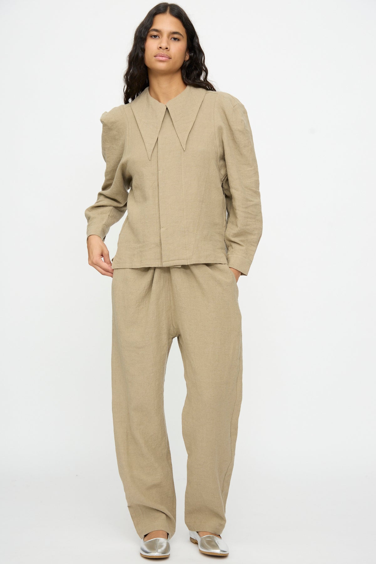 Person wearing a long-sleeved collared shirt and matching loose-fitting Cosmic Wonder Wrap Pants in beige.