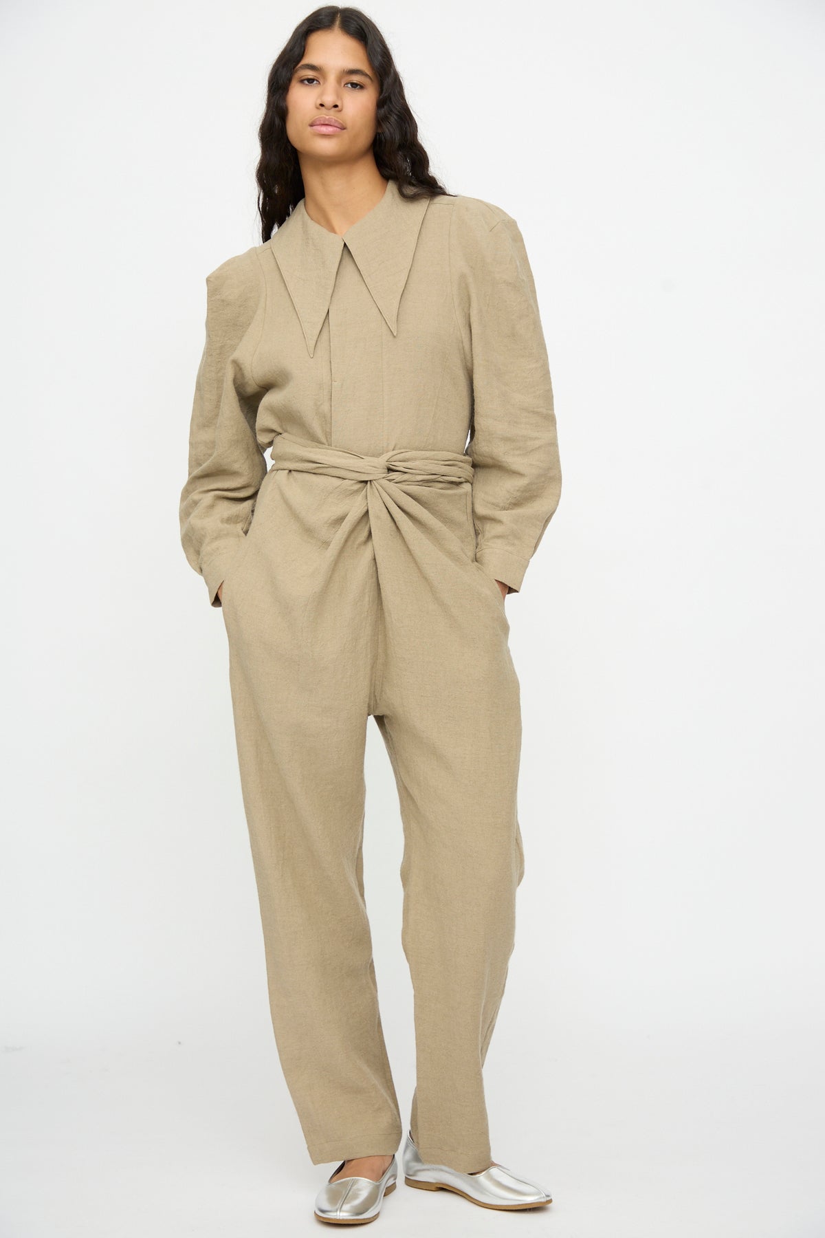 A person wearing a beige, linen Wrap Pants in Beige jumpsuit with a pointed collar and silver flats.
