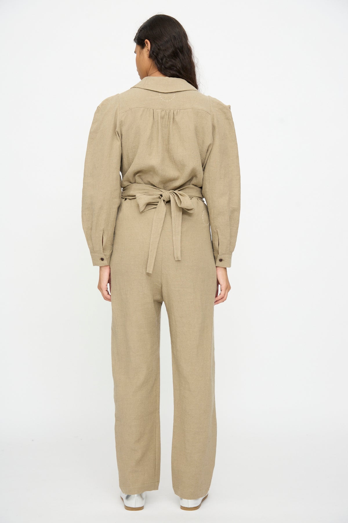 A person seen from behind wearing a beige long-sleeved wool blend Wrap Pants in Beige wrap jumpsuit with a tie-waist.