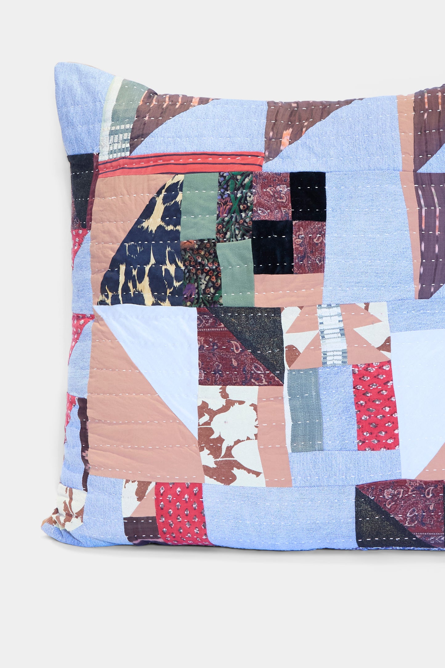 The Patchwork Pillow in Denim and Terracotta Multi I by Counterpane is crafted in California from antique found cloth, featuring a mix of denim, terracotta, and multicolor patterns displayed on a plain background.