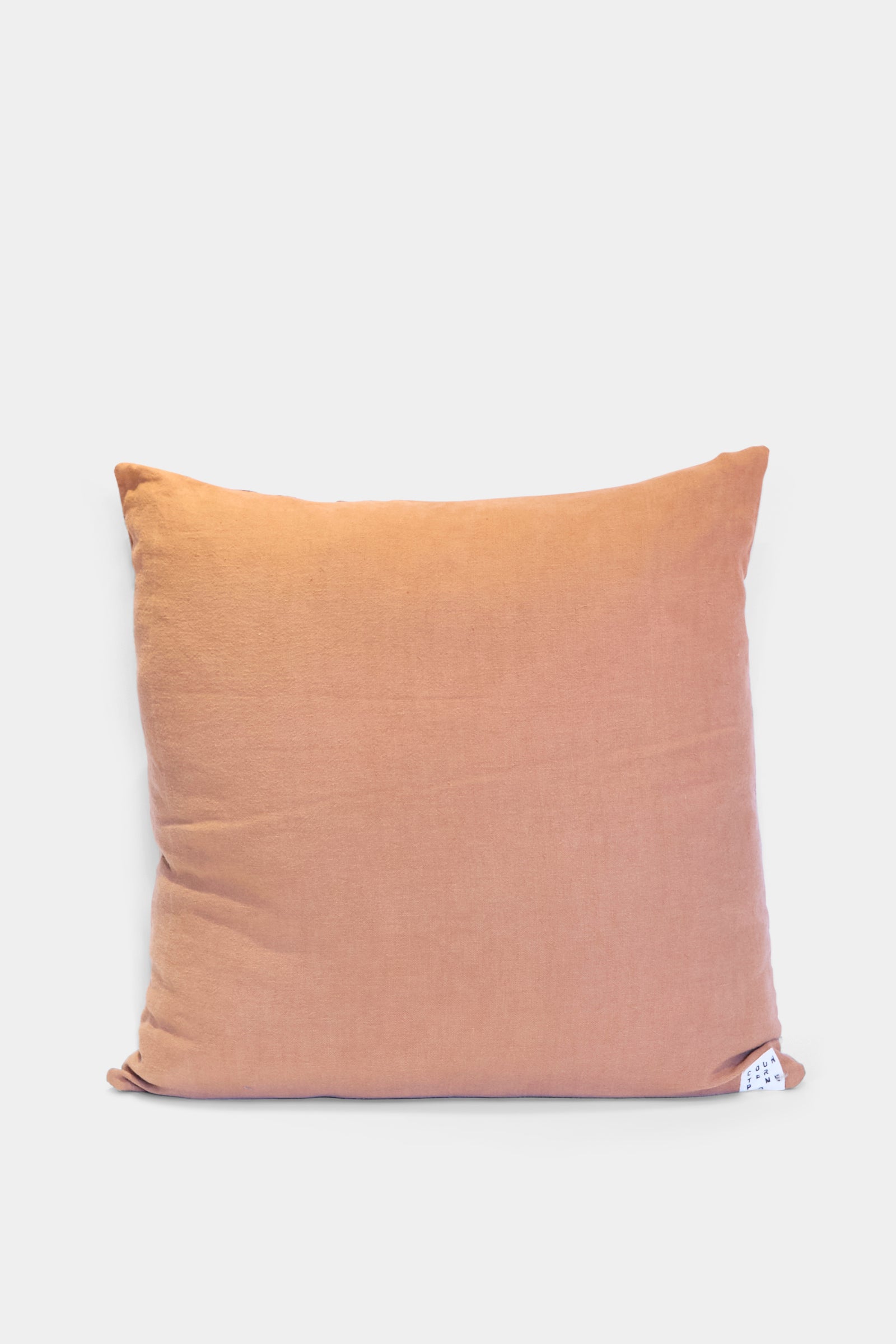 The Counterpane Patchwork Pillow in Denim and Terracotta Multi I is a square, quilted throw pillow in light orange tones with a plain cover and small white tag at the bottom right, beautifully crafted in California, shown on a white background.