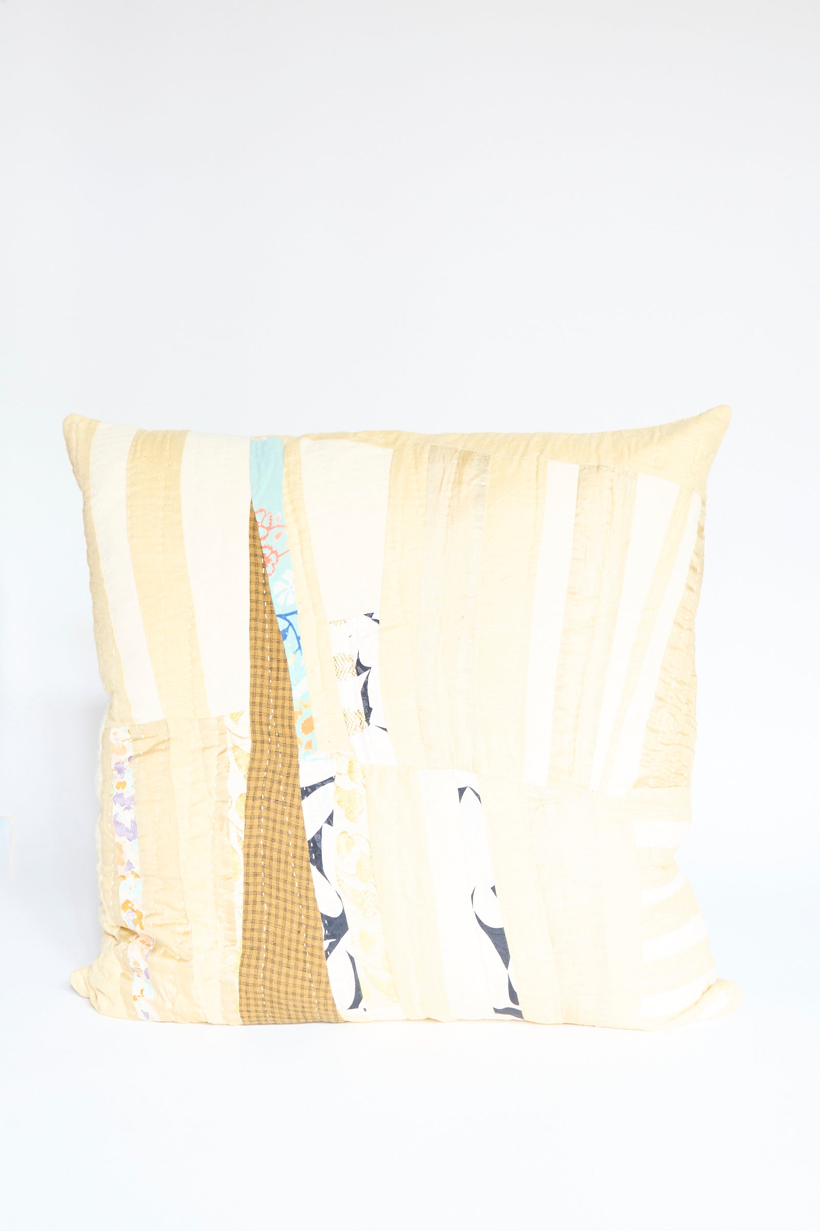 The Counterpane Patchwork Pillow in Gold Multi II features a square quilted design with light yellow, white, mustard, and patterned antique cloth set against a plain white background.