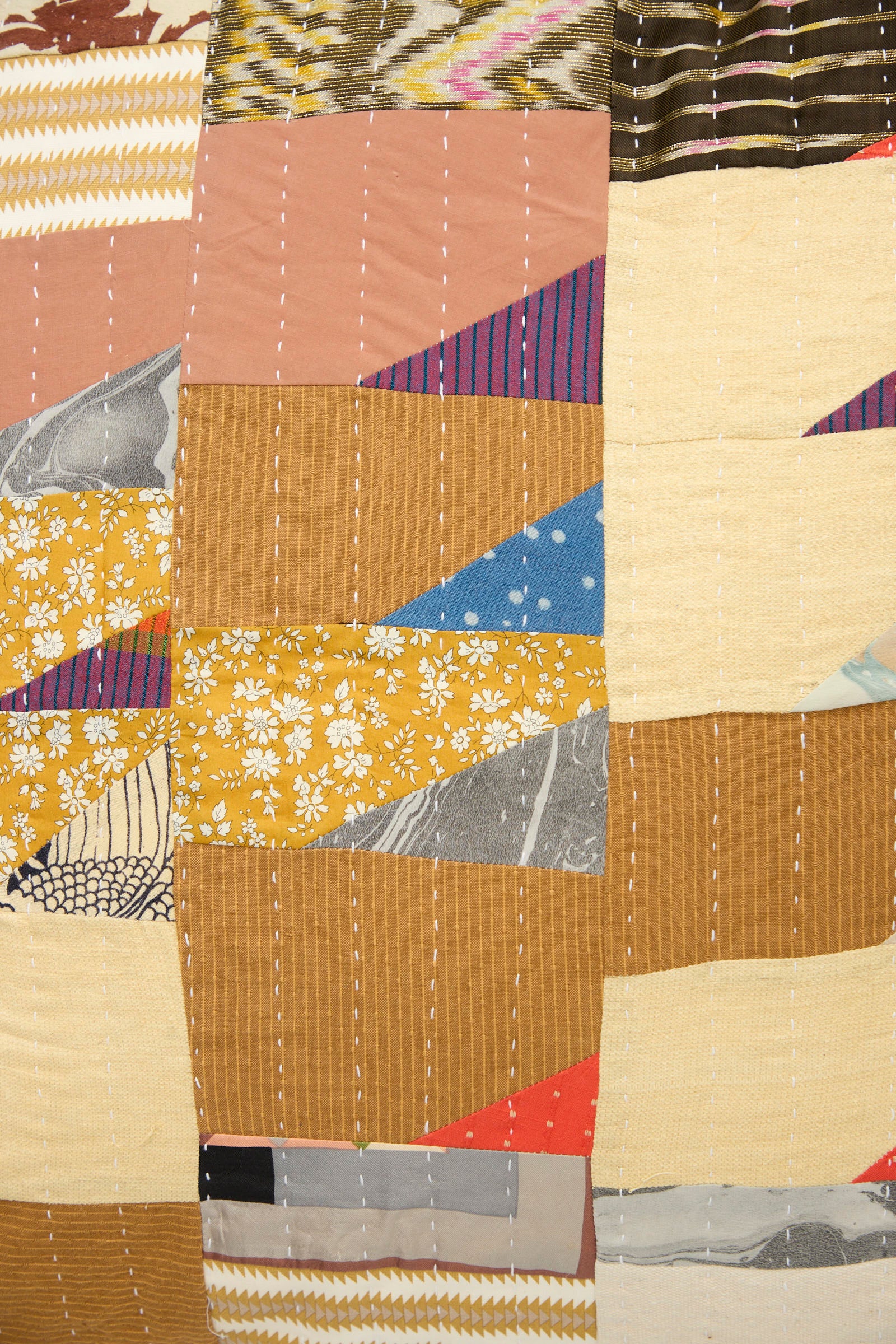 The Counterpane Patchwork Pillow in Earth Multi I features rectangular pieces of patterned fabric in shades of mustard yellow, blue, pink, cream, gray, and white—evoking antique cloth—stitched together with vertical white lines. This design channels the charm of a handmade quilted throw pillow and infuses any space with a touch of California craftsmanship.