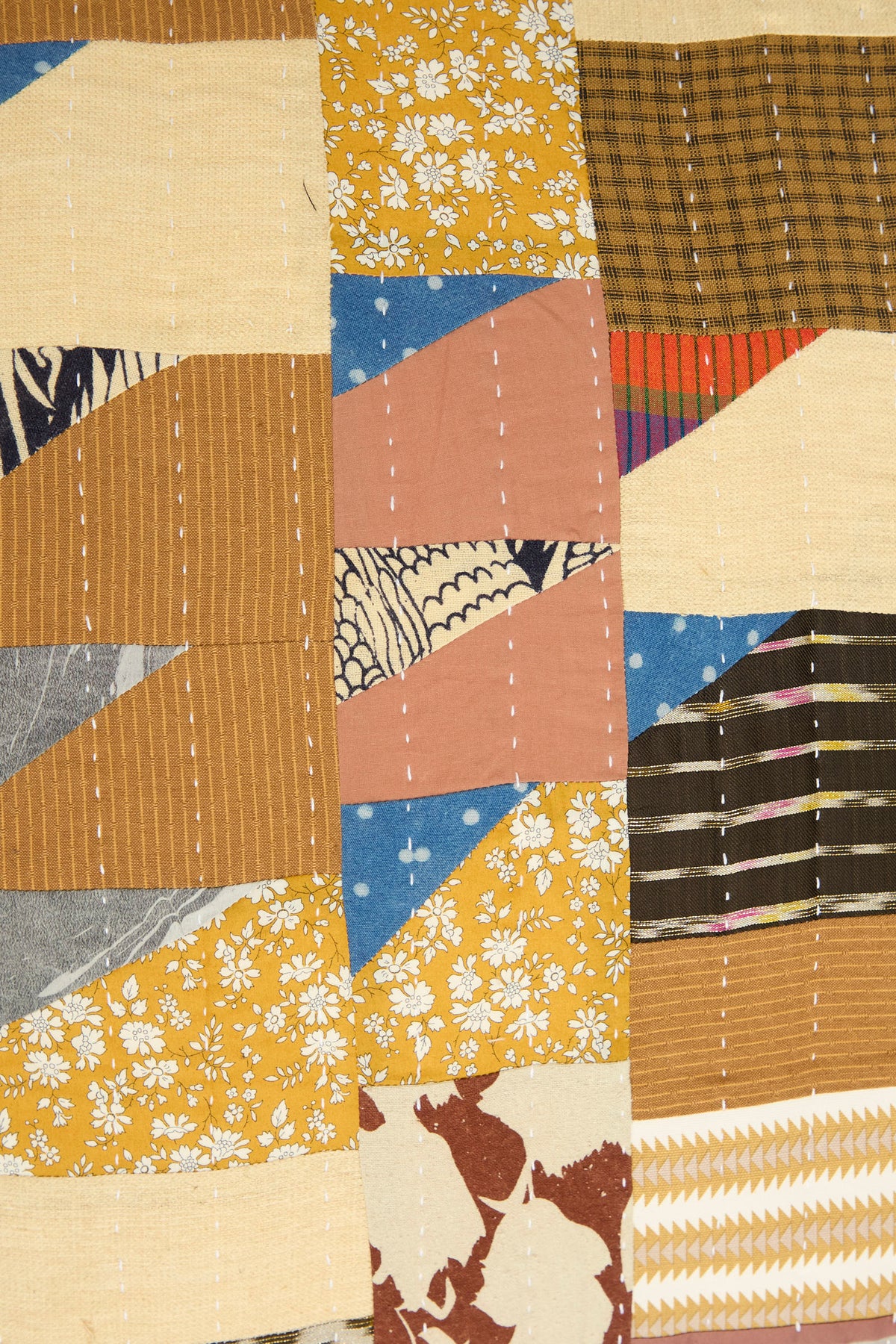 A close-up of the Counterpane Patchwork Pillow in Yellow Gold Multi II, featuring various patterned and solid fabric pieces in yellow, brown, blue, and pink with visible white stitching lines—crafted from antique found cloth and made in California.