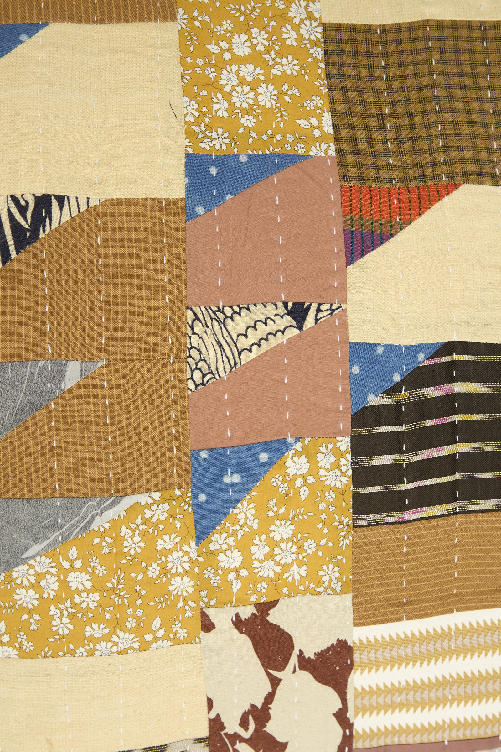 A close-up of the Counterpane Patchwork Pillow in Yellow Gold Multi II, featuring various patterned and solid fabric pieces in yellow, brown, blue, and pink with visible white stitching lines—crafted from antique found cloth and made in California.