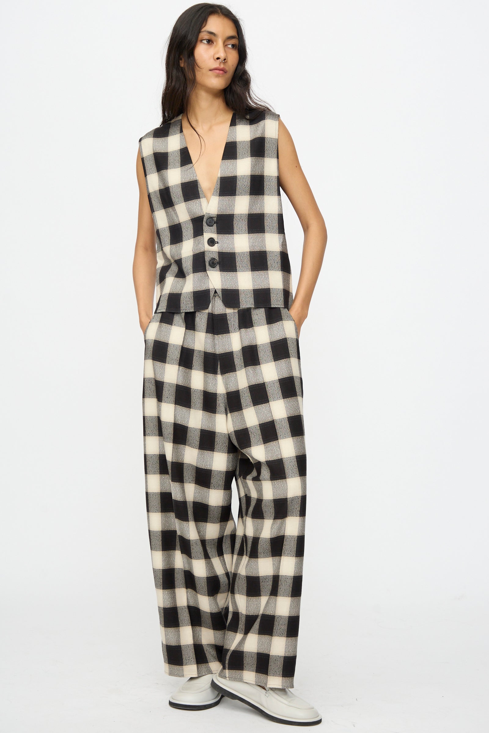 A person wears the Cristaseya Button Down Vest in Black and Cream Checks, a sleeveless cropped bouclé piece, with matching wide-leg checked trousers and light shoes, standing against a plain background.