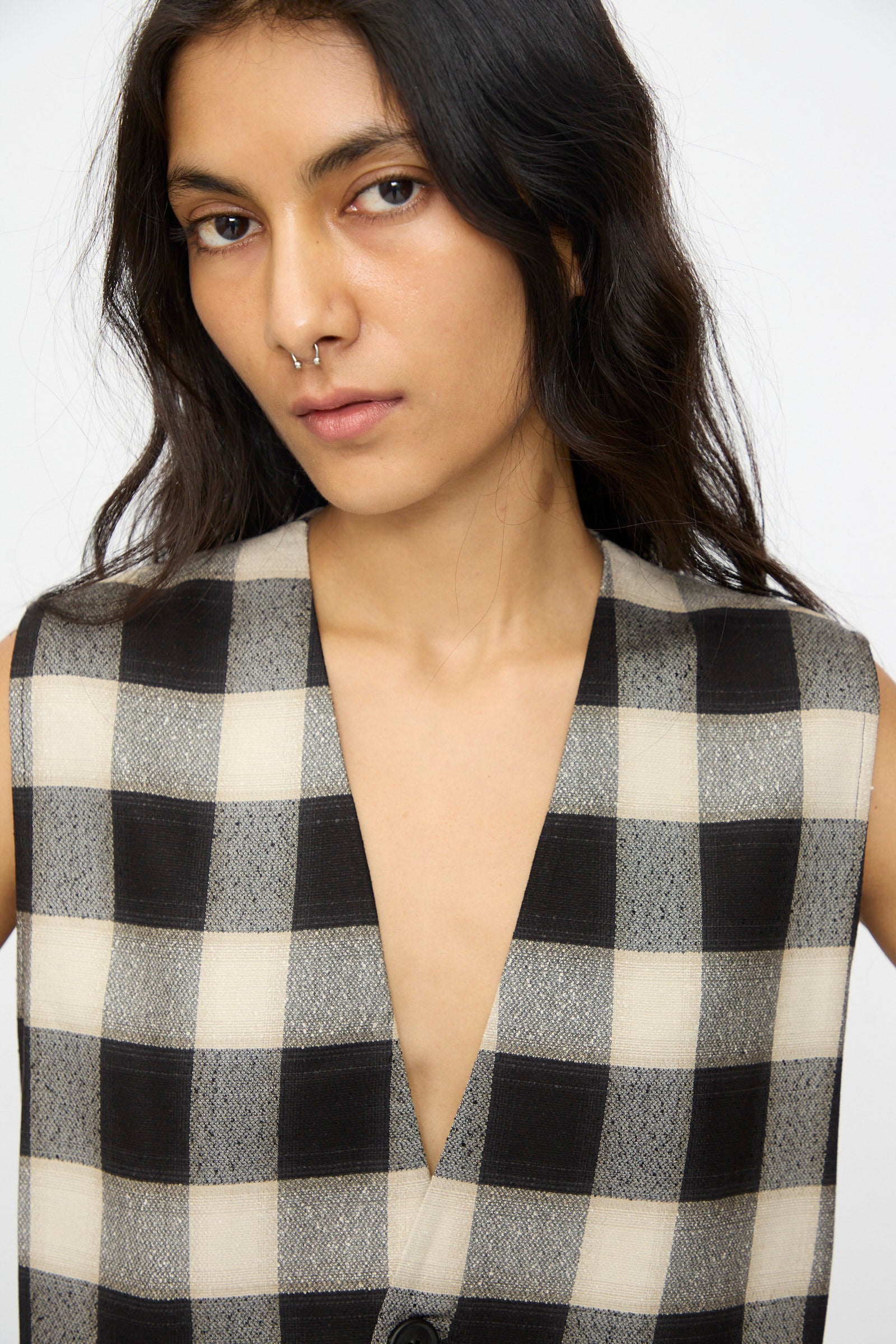 A person with long dark hair and a nose ring wears the Cristaseya Button Down Vest in Black and Cream Checks.